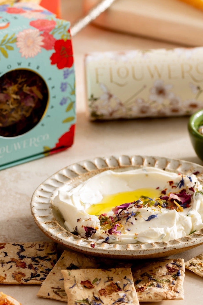Dish of yogurt with honey and dried flowers, crackers, and a floral tea box on a table. ©Flouwer Co.