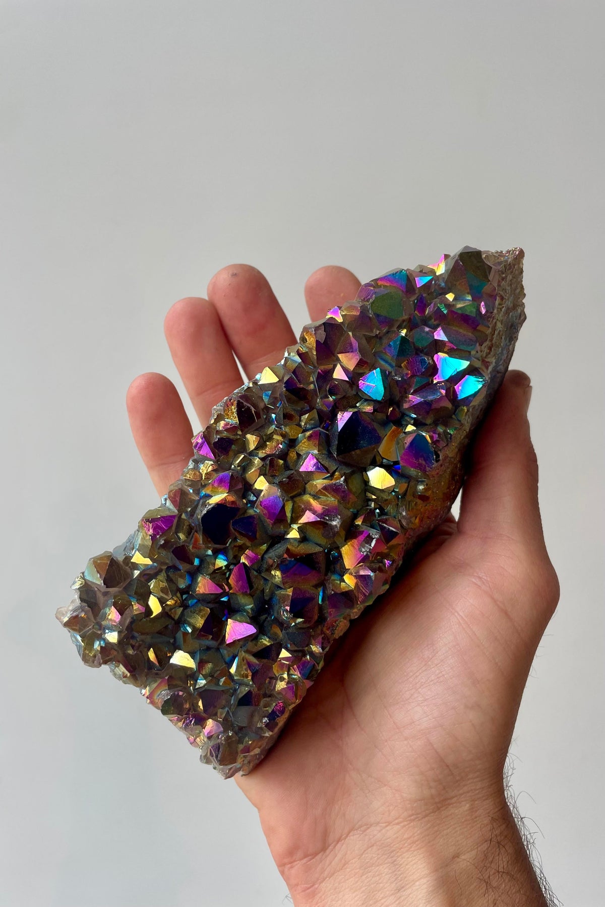 A hand holds a large crystal of colorful amethyst in front of a white wall ©Sprout Home