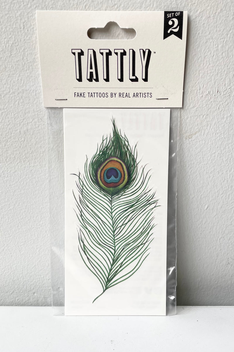 The peacock feathers tattoo in its Tattly packaging against a white wall. 