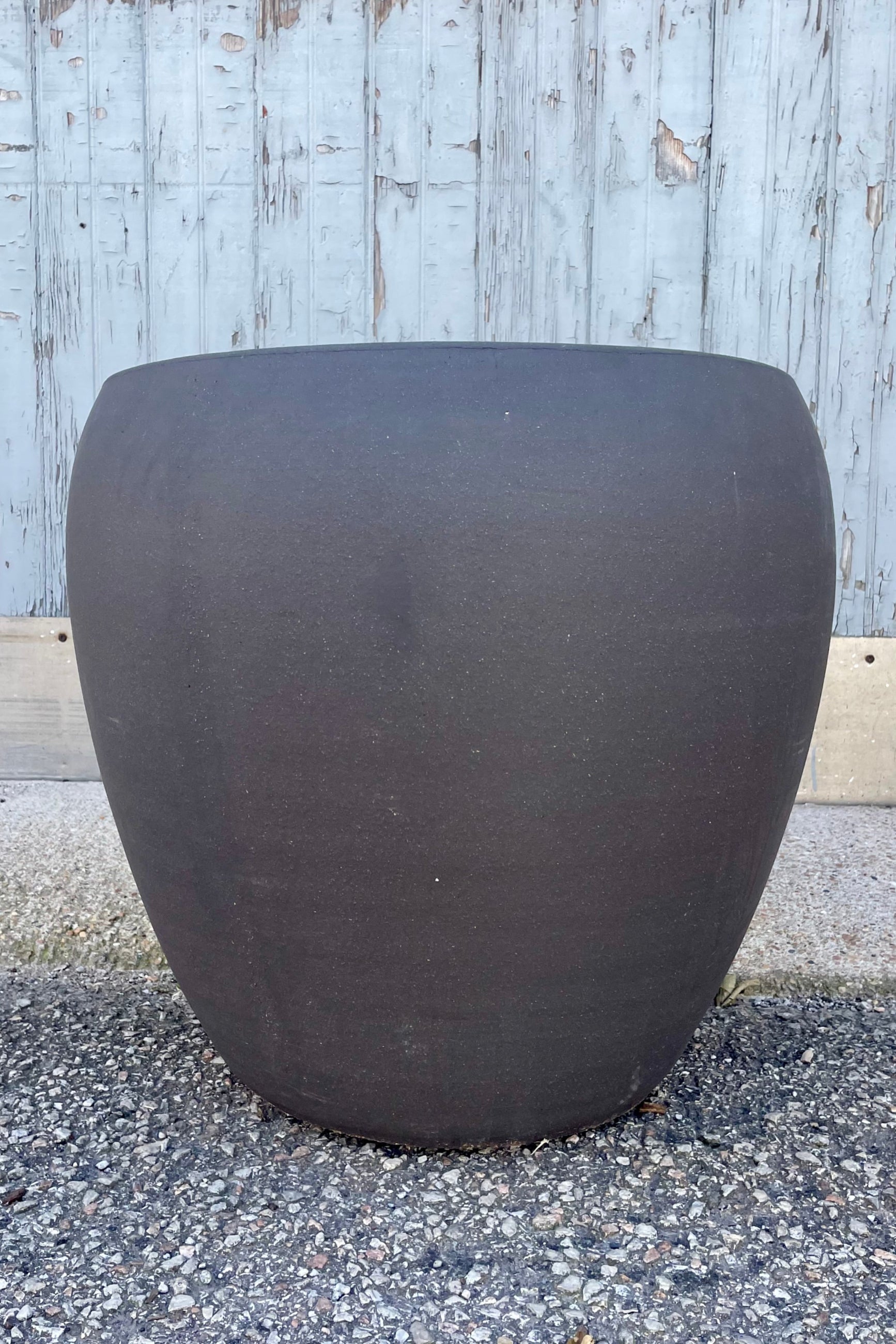 Photo of a rounded brown planter on a gravel surface in front of a textured wall ©Sprout Home