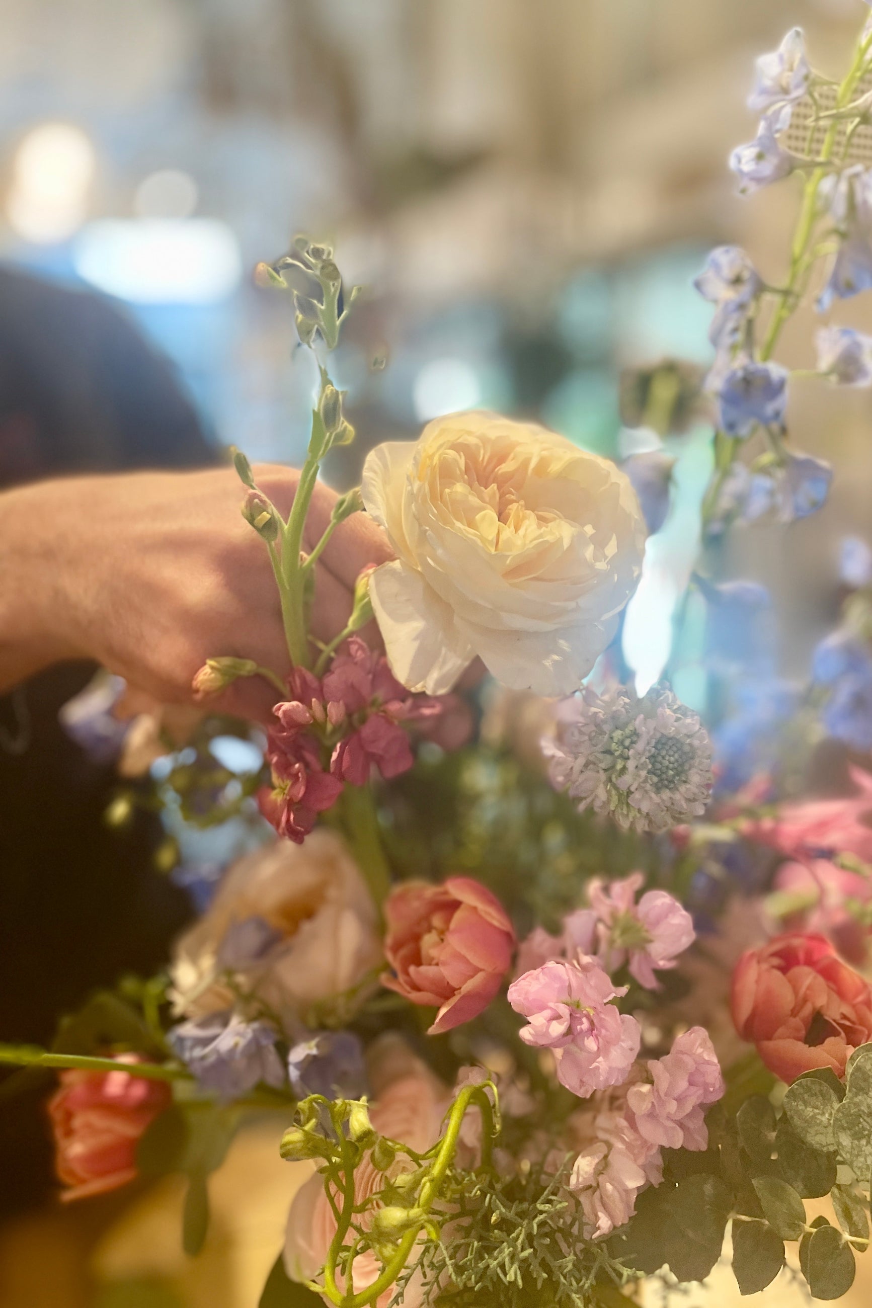 Close-up of a hand arranging a bouquet of colorful flowers with a blurred background ©Sprout Home