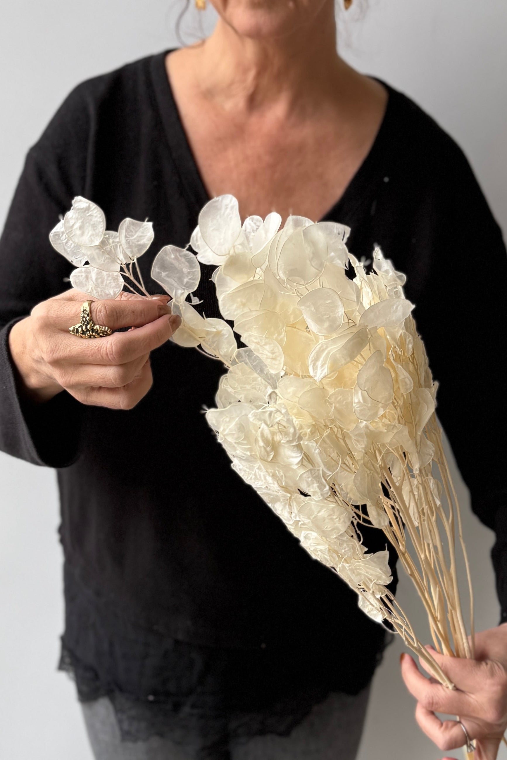 Person holding a bouquet of white dried Lunaria against a neutral background ©Sprout Home