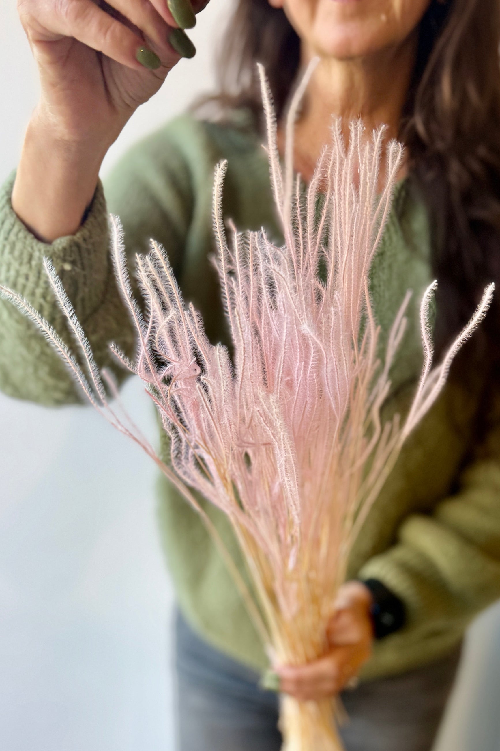 Person holding a bundle of blush colored preserved Ouro against a neutral background ©Sprout Home