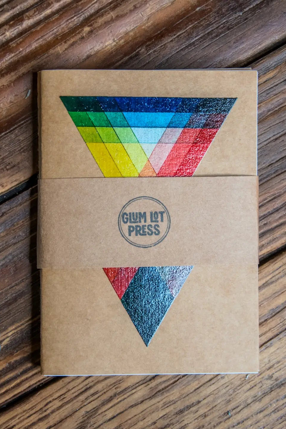 Notebook with colorful triangle design as part of the Color Theory Pack Travel Journal 3 Pack Notebooks on wooden surface ©Glum Lot Press