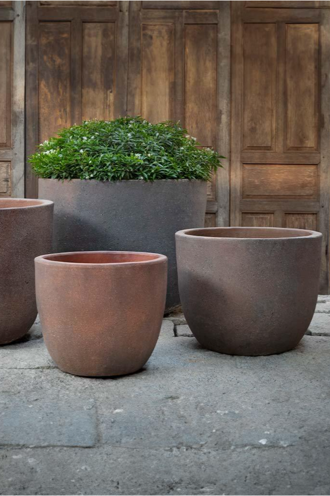 A set of four sandblasted terracotta Saba Planters in front of a wooden wall. The second largest side is half visible from the left side of the photo. All other planters are in full view from the side. ©Campania