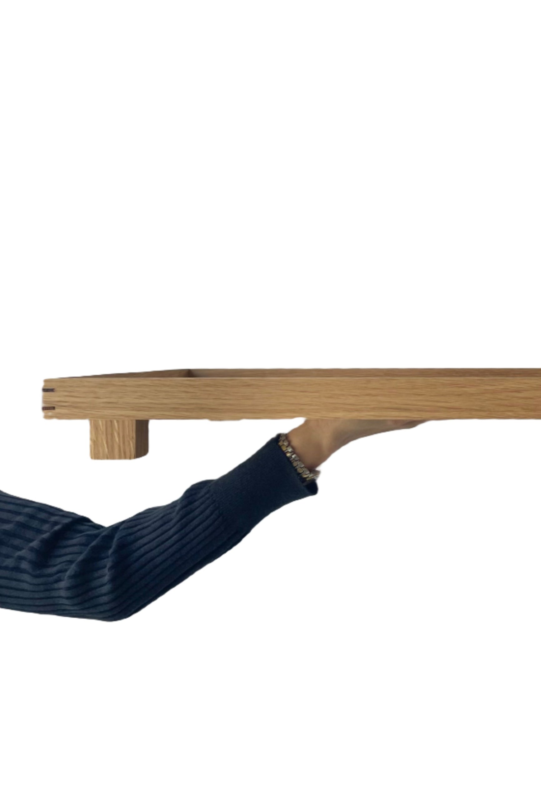 Photo of a Ferm Living Bon Wooden Tray held in front of a white wall. The side and legs of the tray are shown. ©Sprout Home