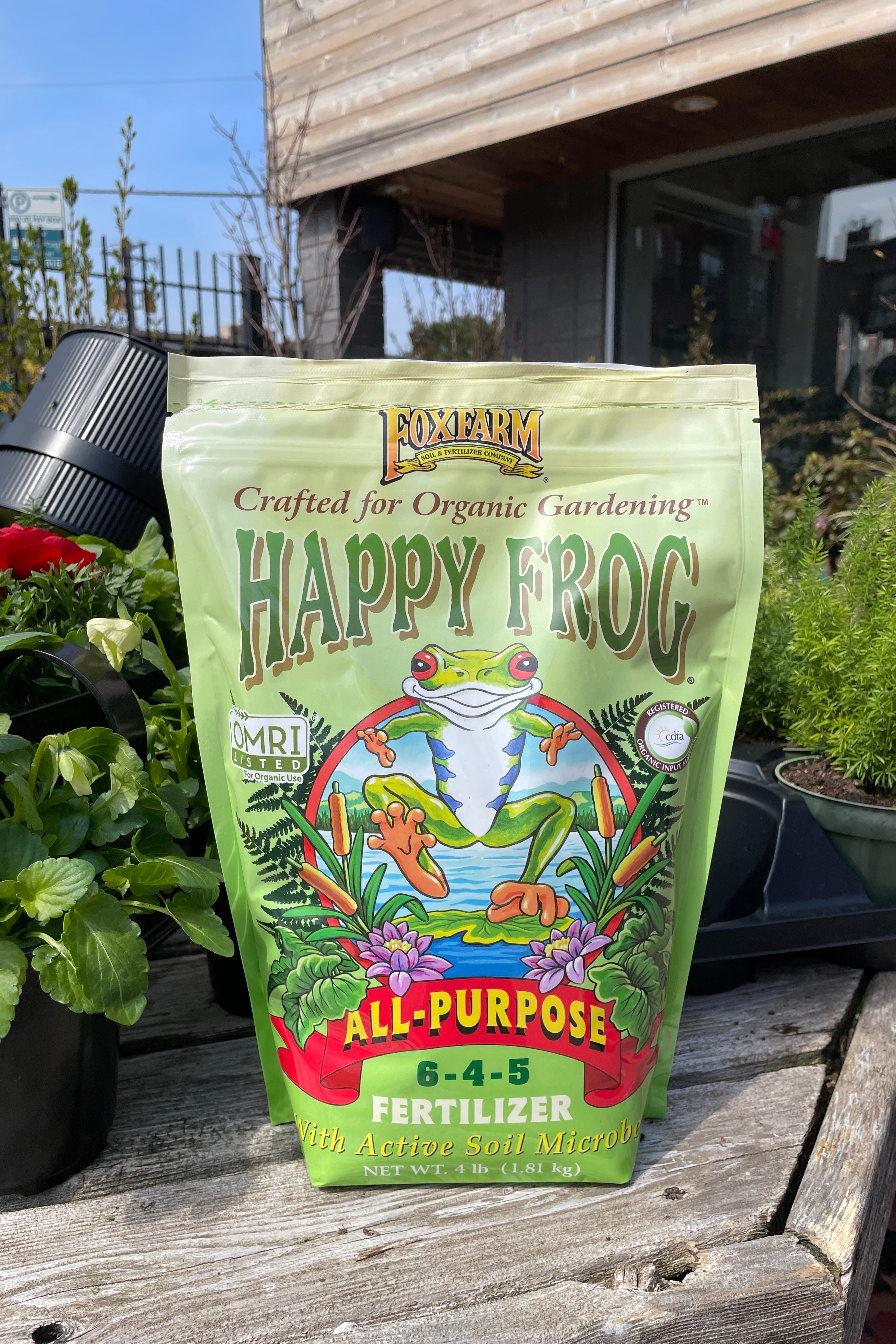 Happy Frog All purpose fertilizer 4lb bag sitting on a table with plants in the Sprout Home yard.