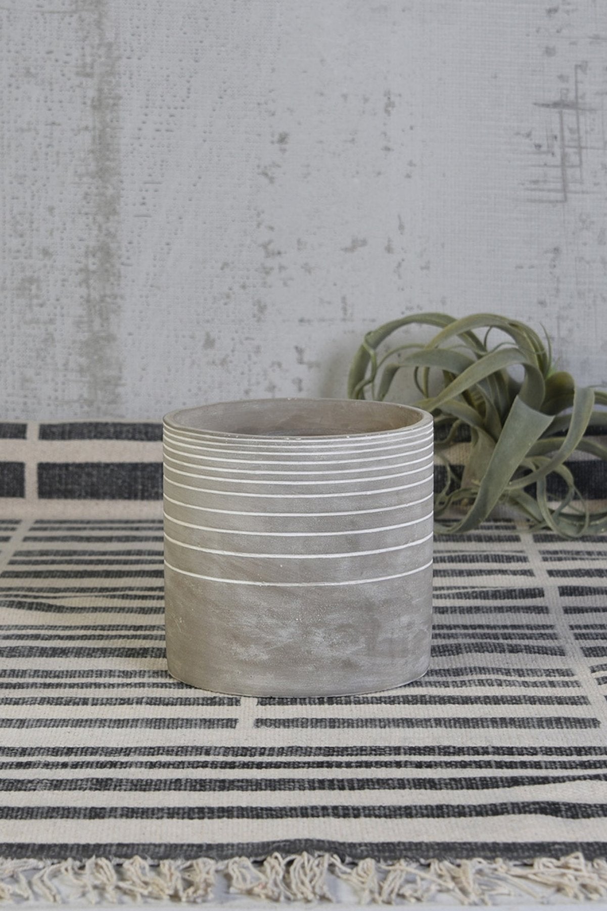 Paso Linear cement cachepot by Homart on a black and white striped cloth with an airplant behind it.