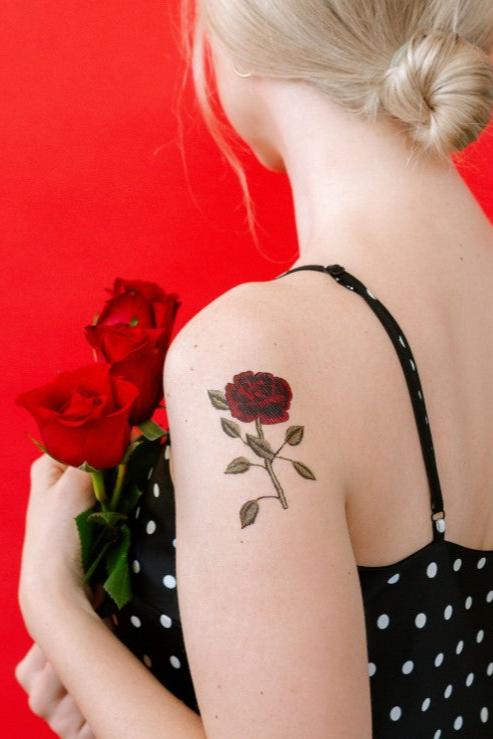 Stitched Rose Tattoo by Tattly being worn by a blond haired woman in a black and white polka dot dress with a red background.