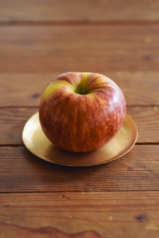 Medium Brass Plate by Fog Linen Work sitting on a wood surface and one apple on top of the plate.