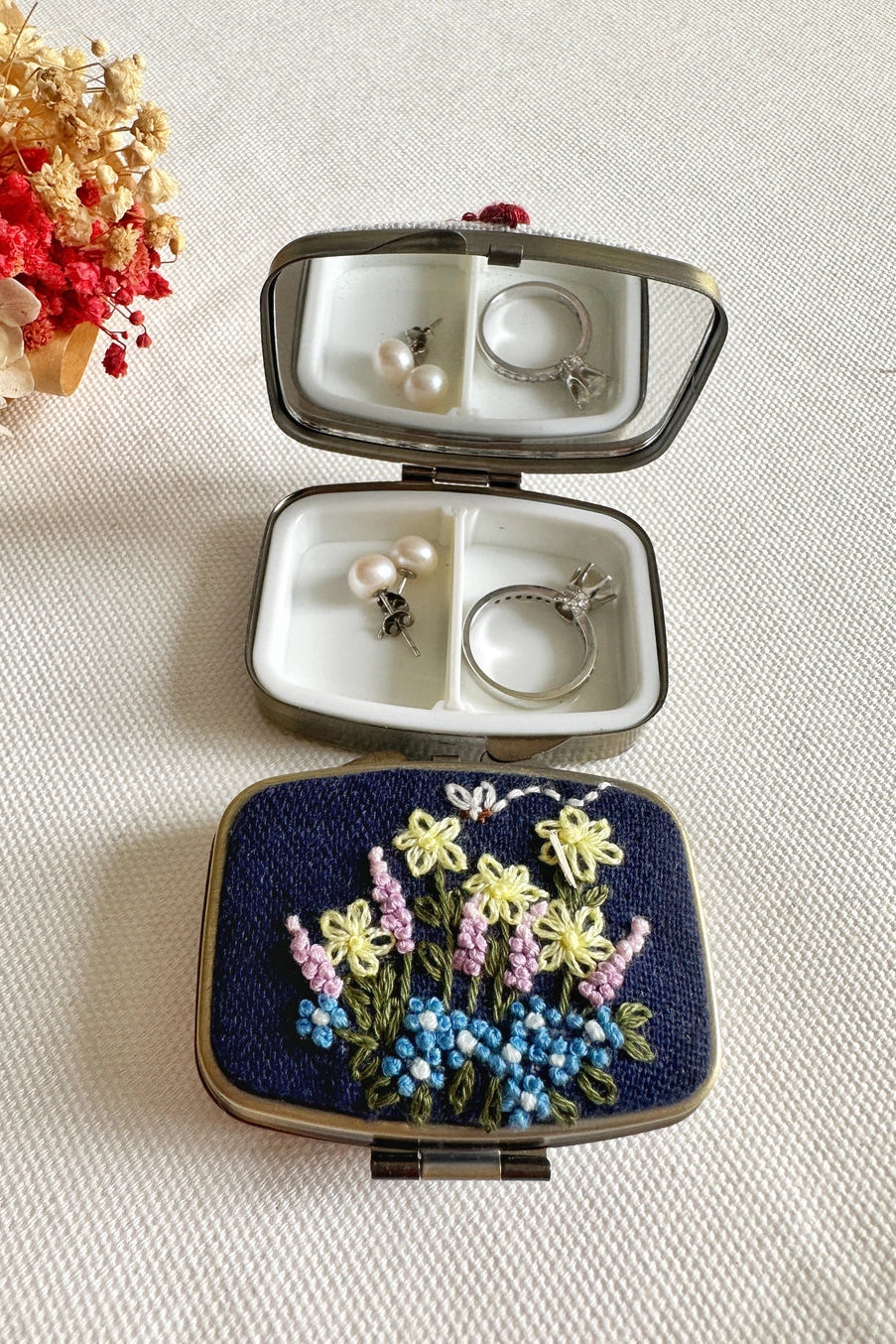 Jewelry case with embroidered lid containing earrings on a light background ©Quince Fables