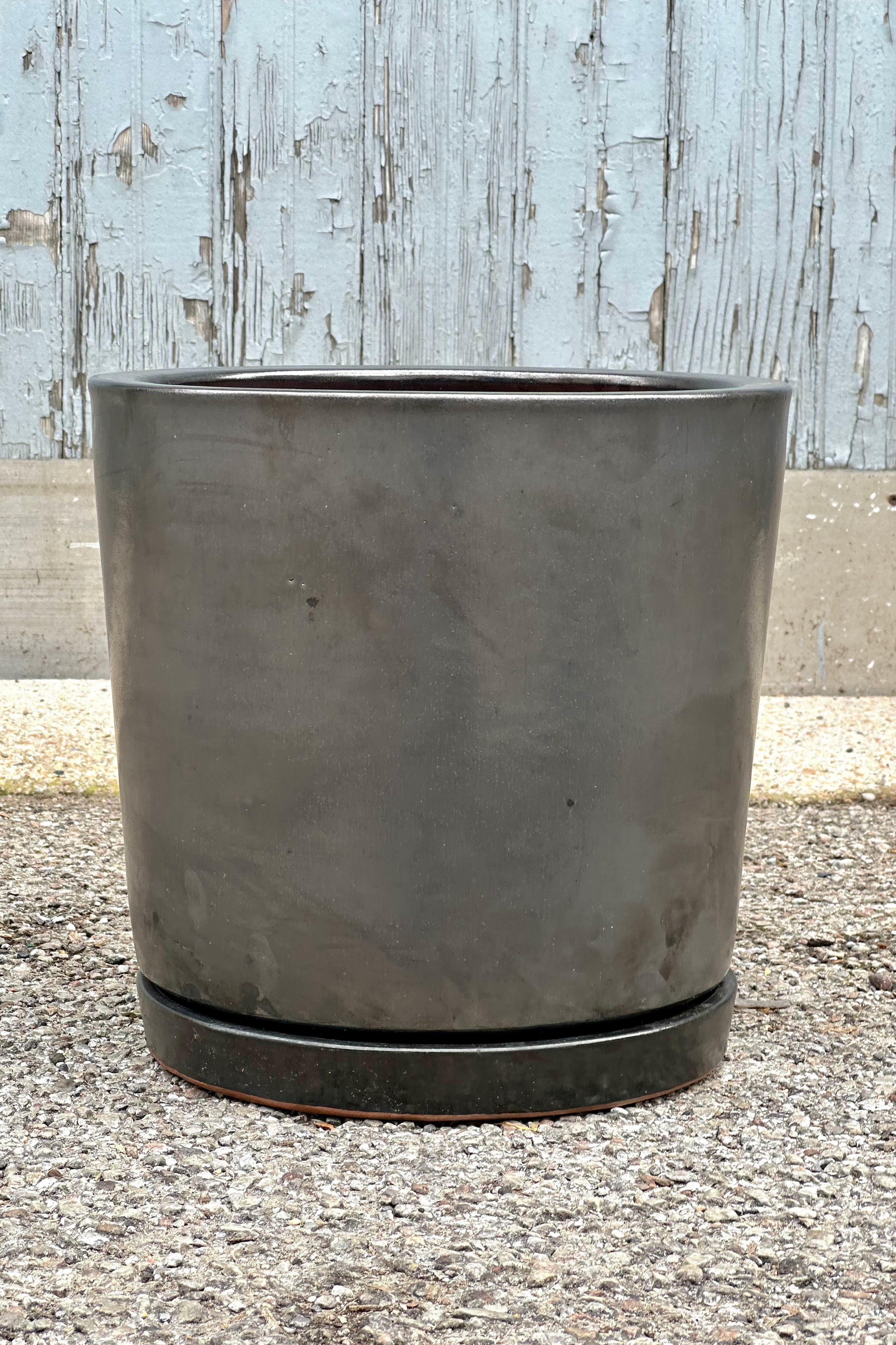 The Graphite cylinder I/O2 planter and saucer shown from the side sitting on a concrete floor