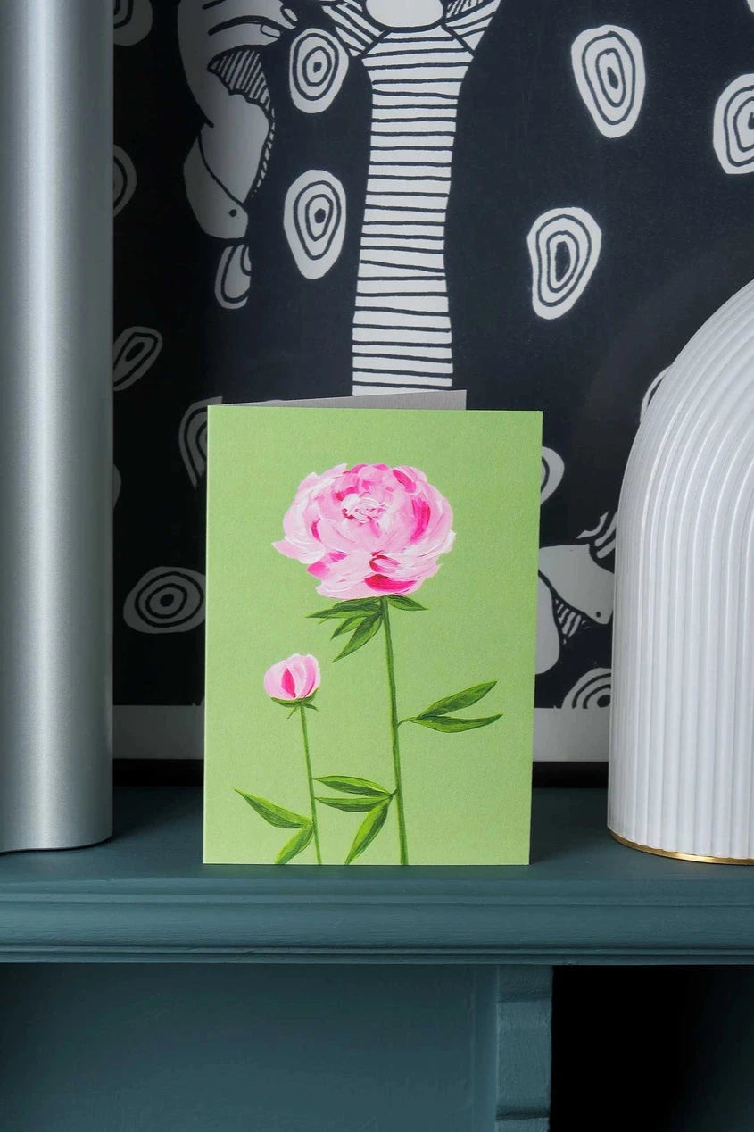 Peony greeting card by Stengun Drawings sitting on a ledge in a lifestyle shot with its two peony flowers on green.