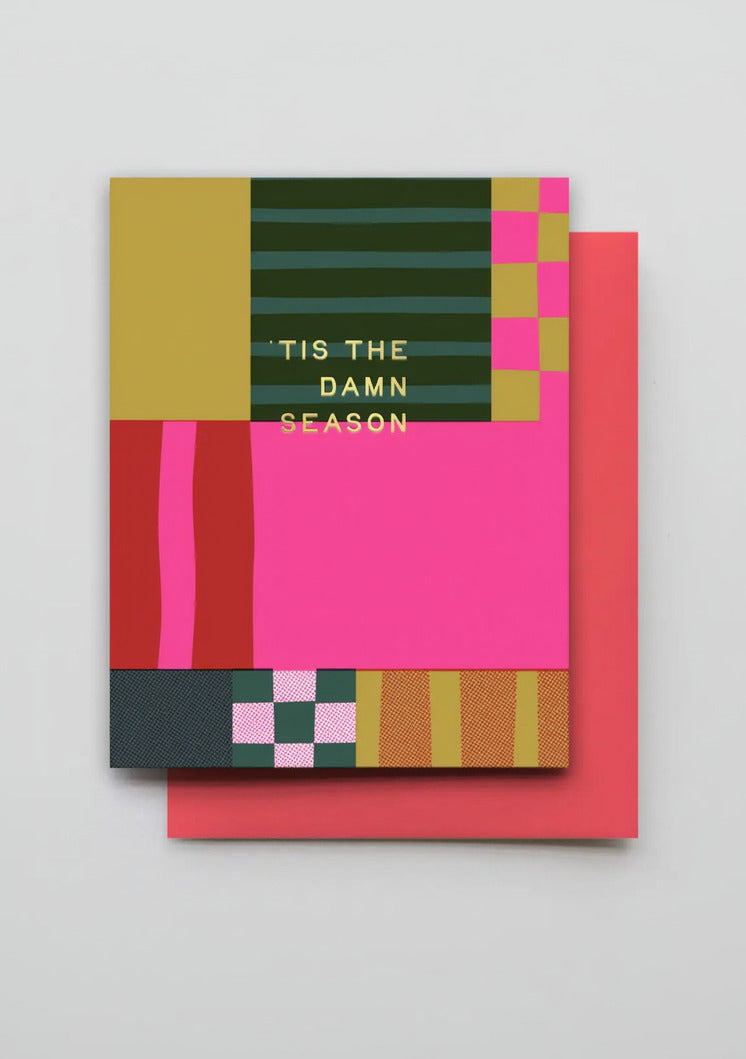 Holiday Season Patchwork Layers Card - Red with a bold abstract geometric design in pink, red, green, yellow, and dark charcoal, with the text 'TIS THE DAMN SEASON' in gold. A coral-red envelope is placed behind it on a light gray background. ©Hammerpress
