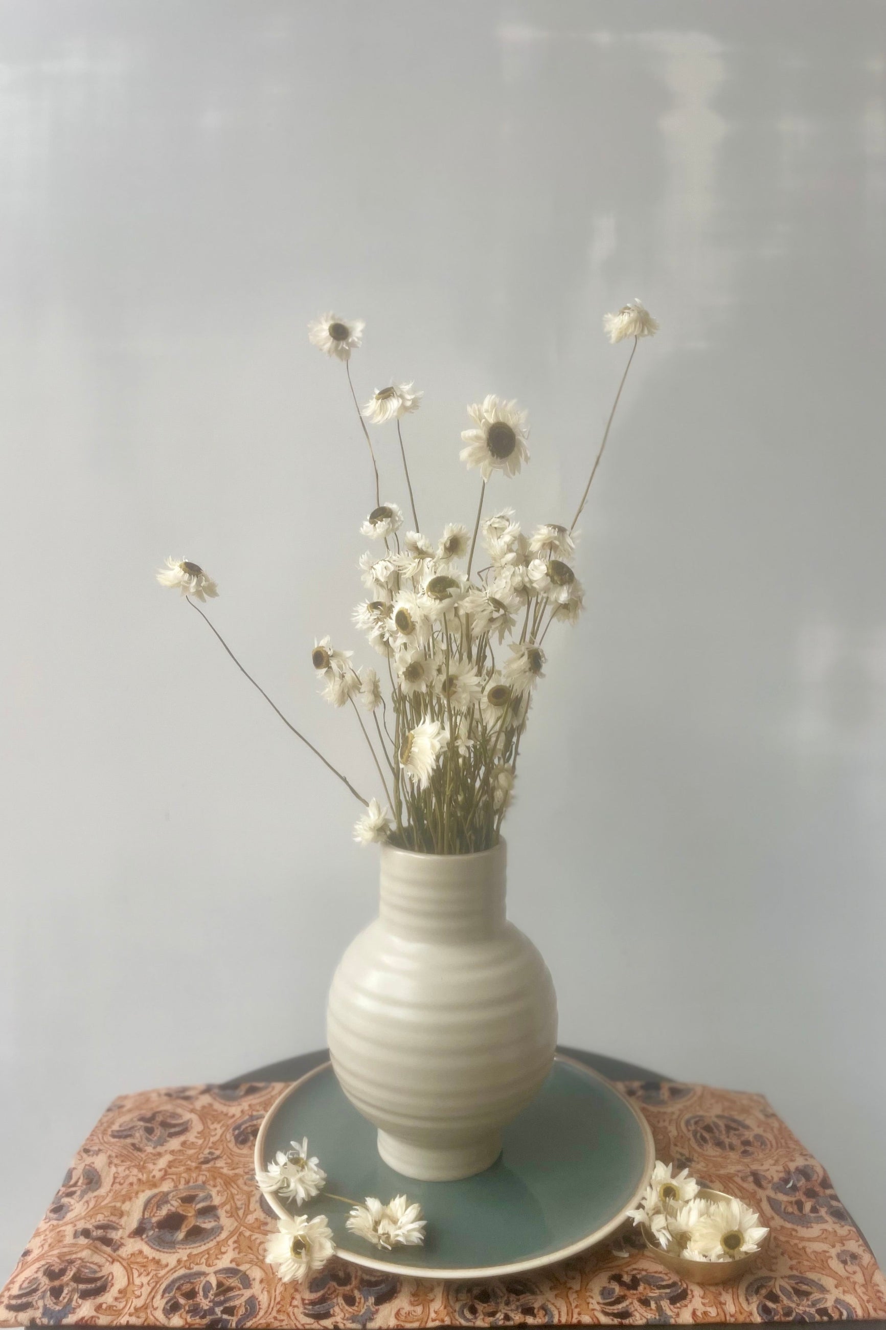 A bundle of white dried flowers in a vase in front of a white wall ©Sprout Home