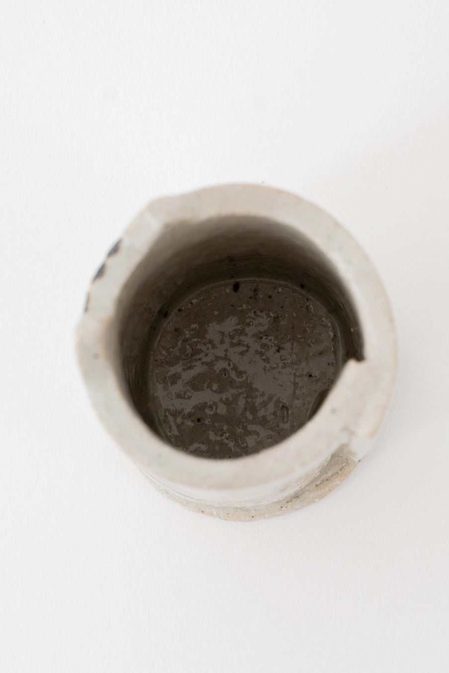 A small handmade ceramic white cat vase with a rough, textured light gray exterior and a dark, glossy interior, shown from a top-down view on a white background. ©Great Zakka