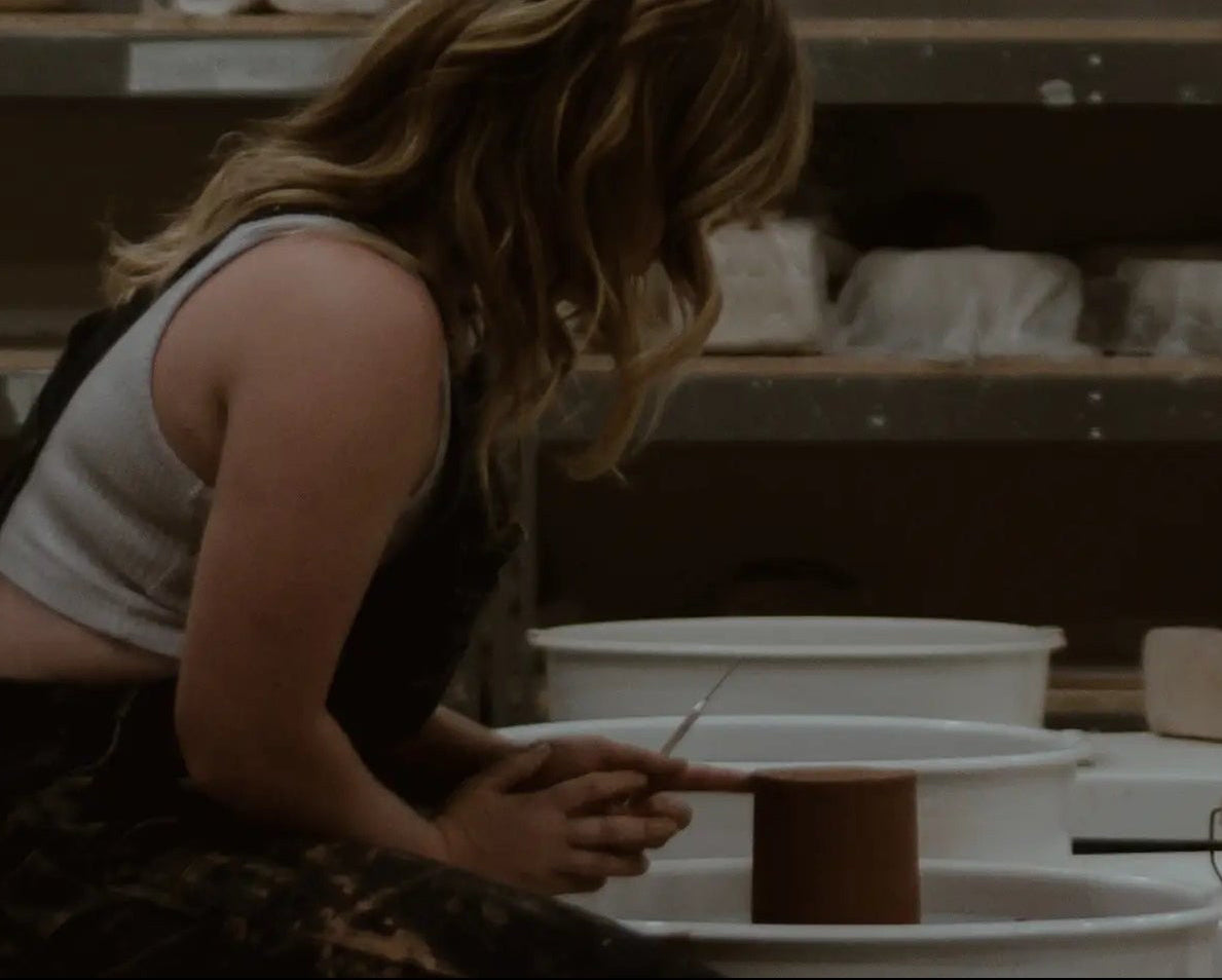 Olivia Snow working with pottery in a studio filled with shelves of ceramic items. ©Olivia Snow Ceramics