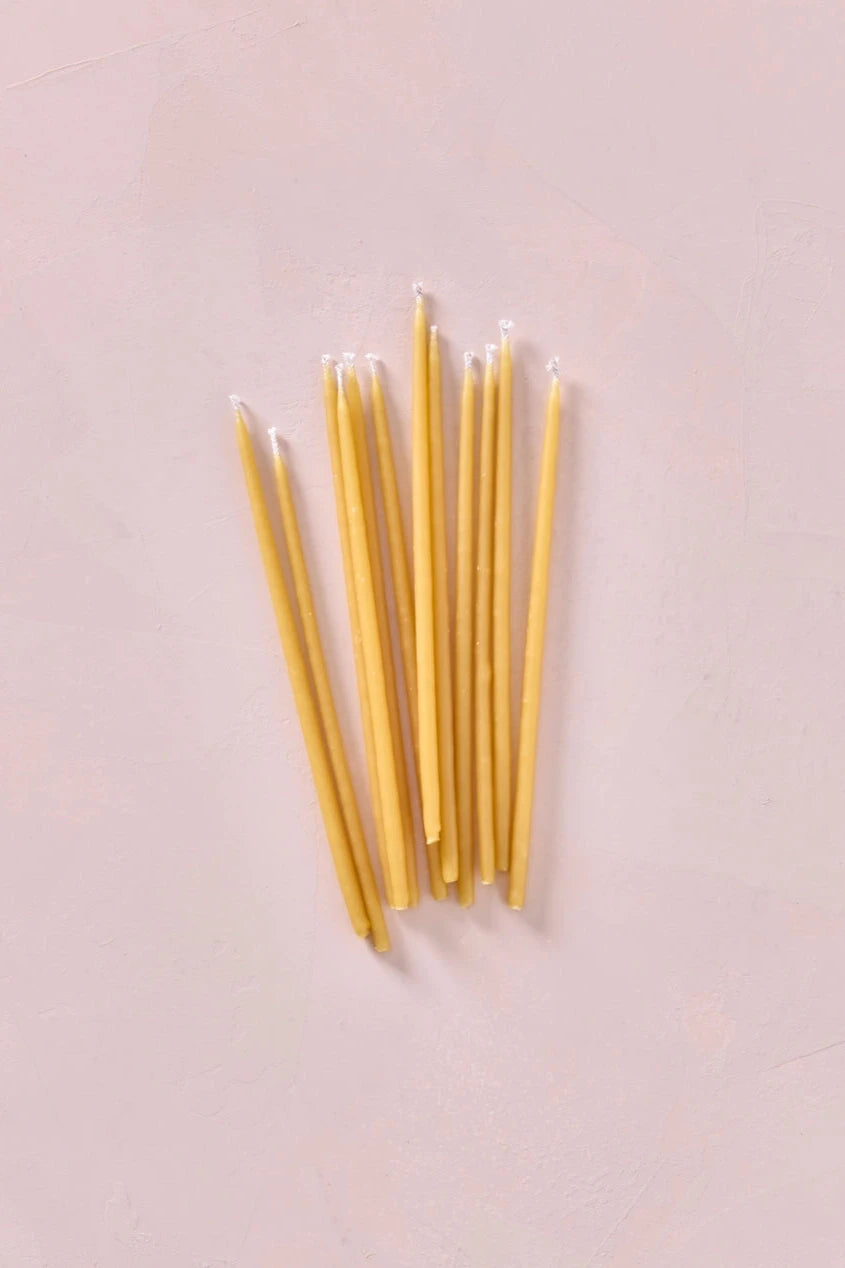 Knot & Bow Tall Natural beeswax candles out of their package and laying down on a pink surface