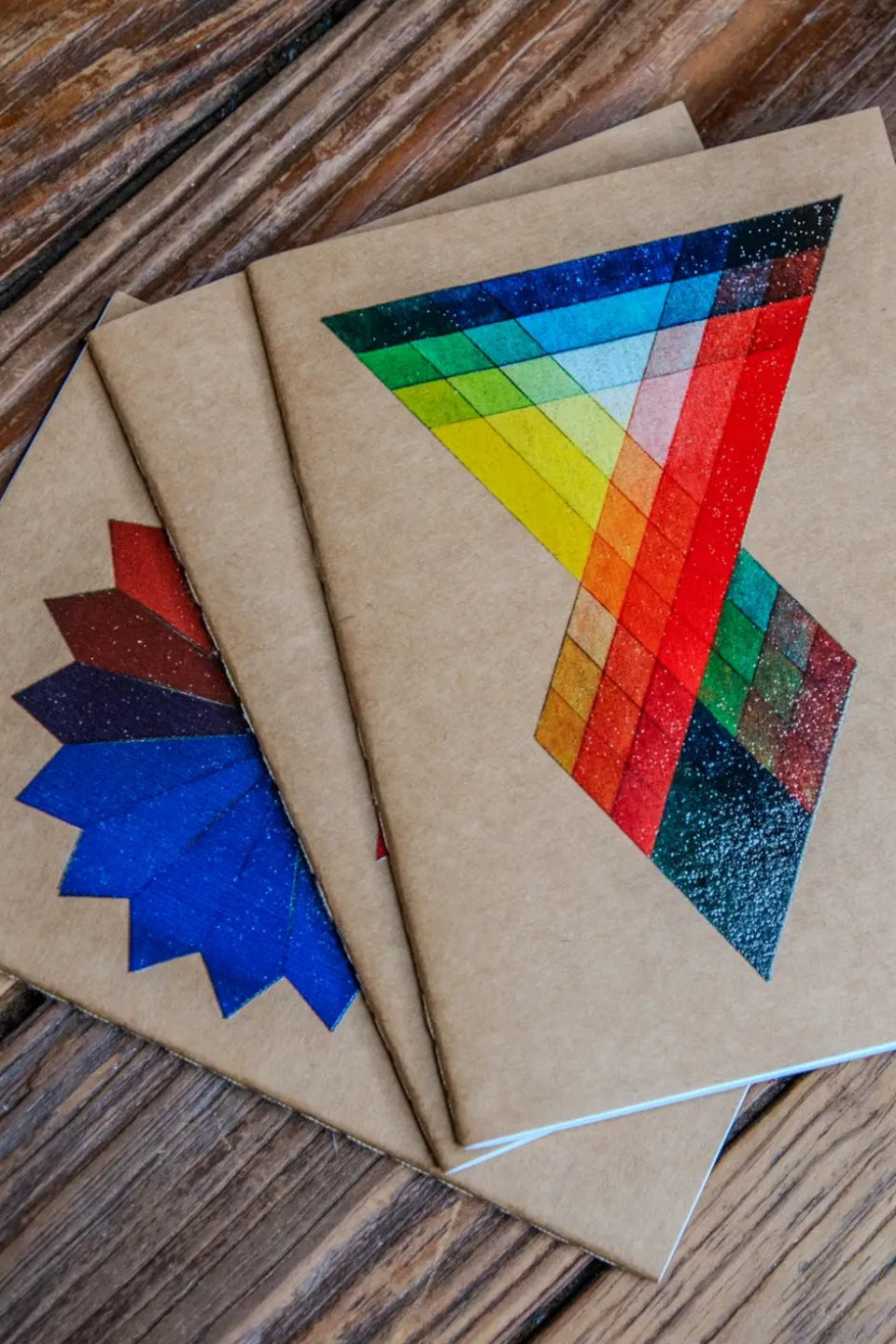 Color Theory Pack Travel Journal 3 Pack Notebooks with colorful geometric designs on a wooden surface ©Glum Lot Press
