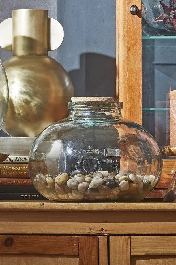 Decorative setting with Olly glass jar filled with stones, a wooden cabinet ©Creation Jute USA