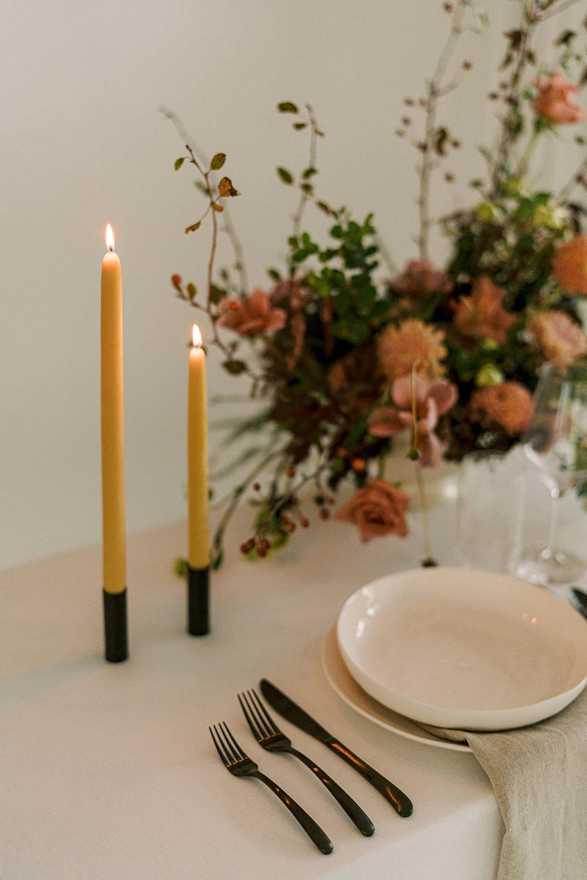 Mo & Co natural gold beeswax candles shown li and part of a table setting with flowers