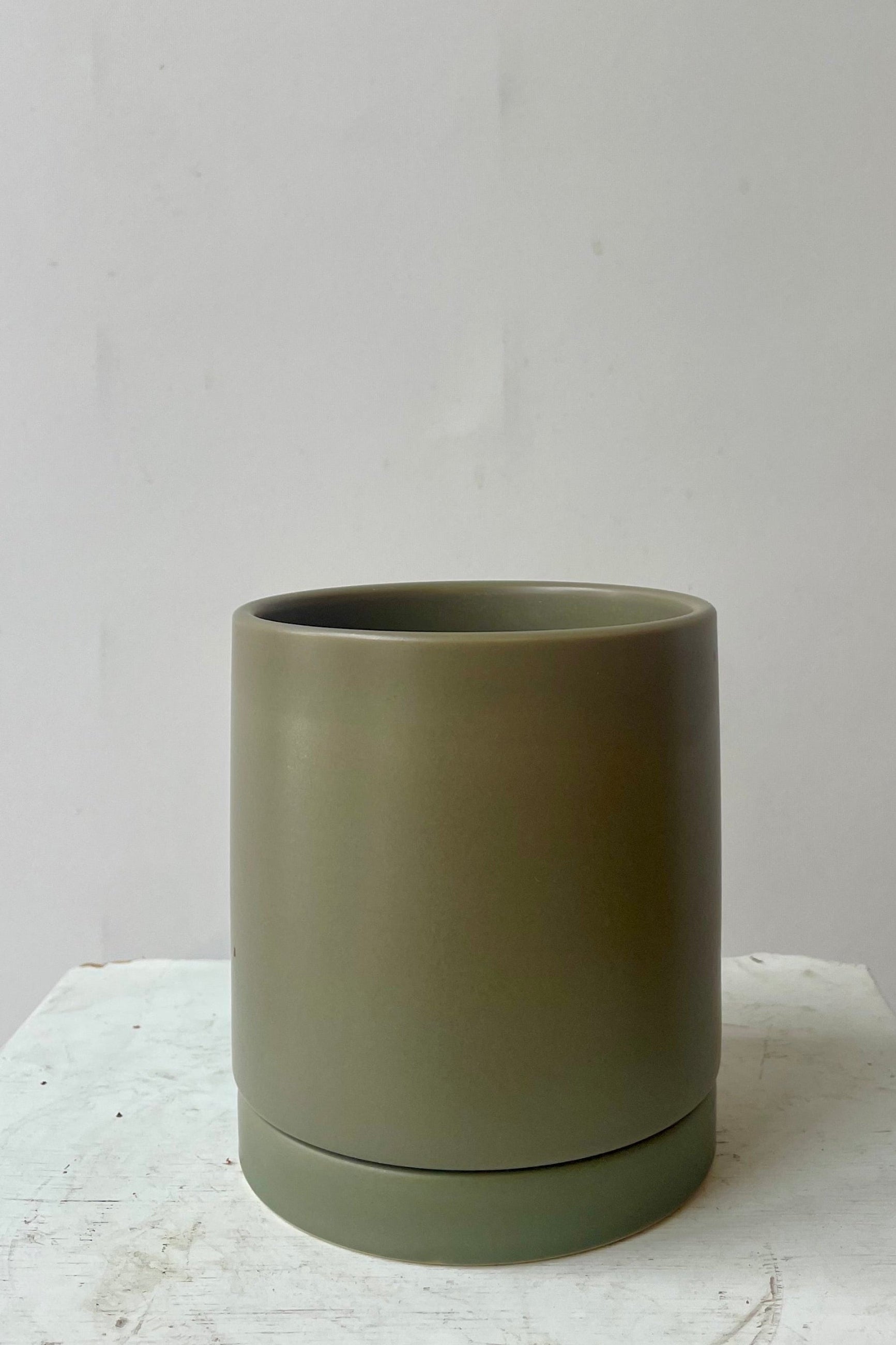 Photo of khaki colored cylindrical pot and saucer in front of a white wall ©Sprout Home