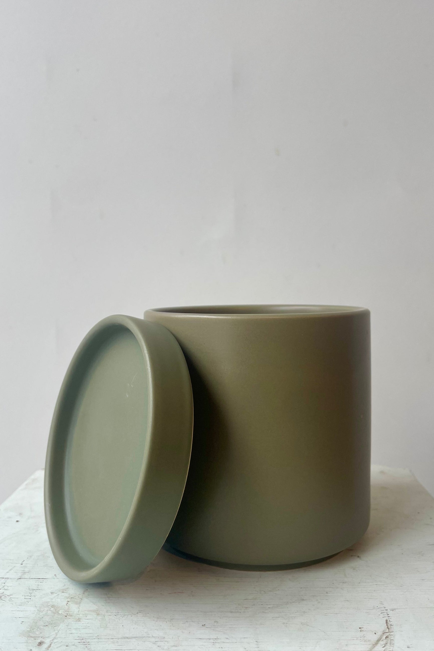 Photo of khaki colored cylindrical pot and saucer in front of a white wall ©Sprout Home