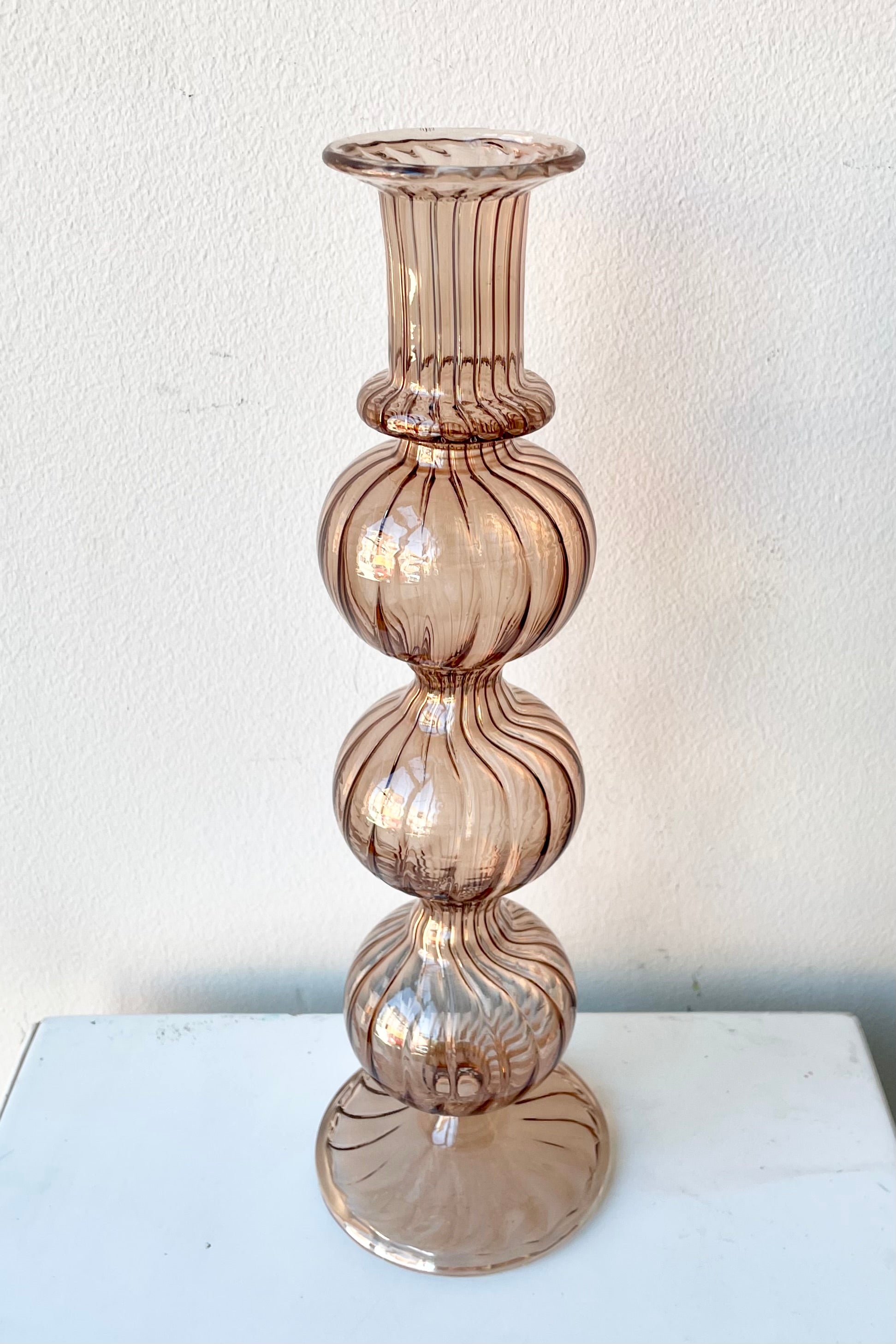 Amaranth Nalia glass candlestick holder against a white wall.
