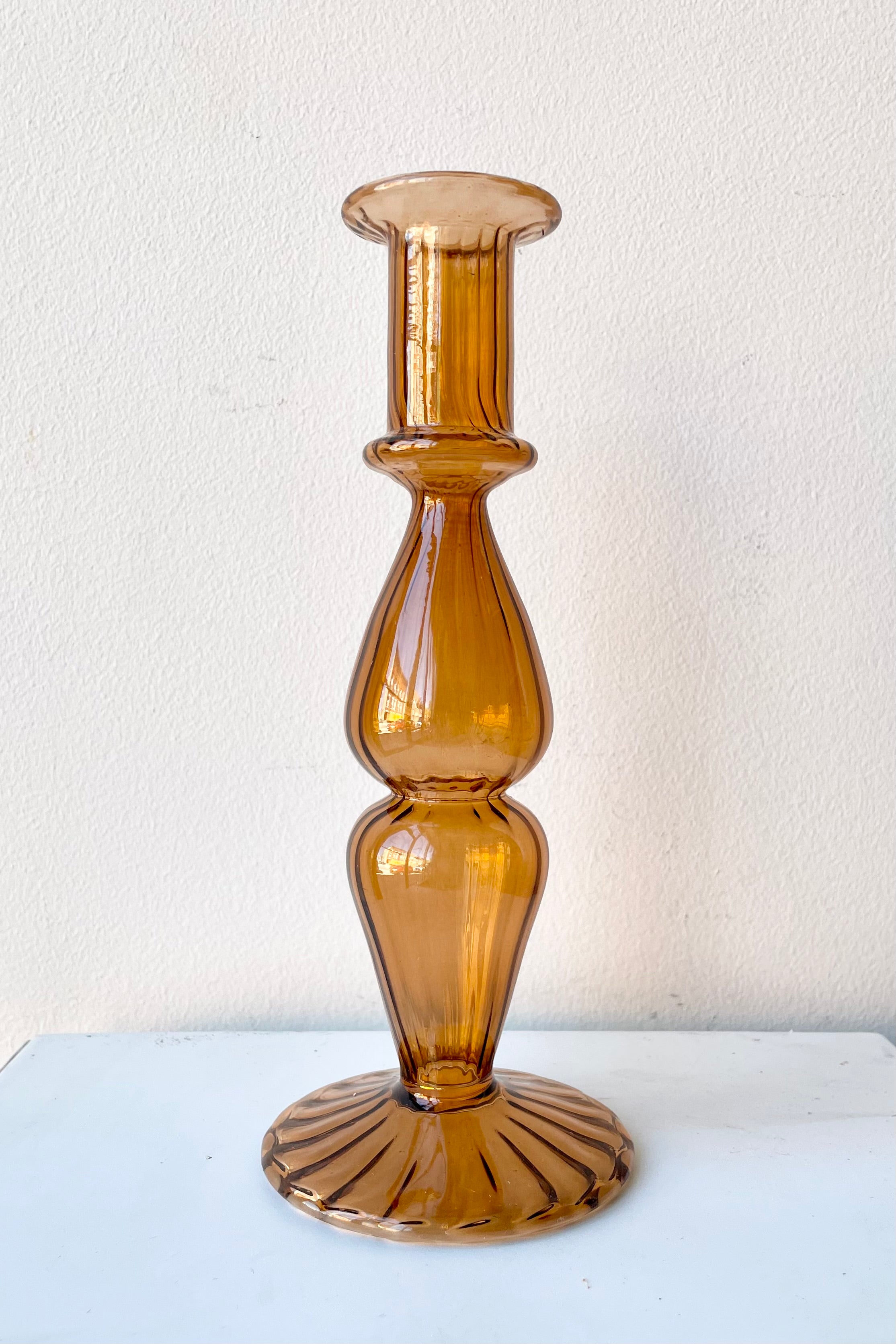 Nalia Glass candlestick holder in Marmalade against a white wall.