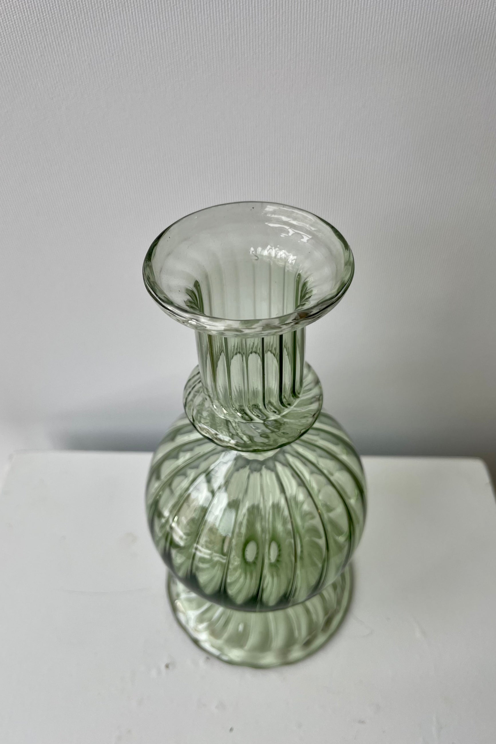 Photo from above of green transparent glass of Nalia Parakeet Candlestick Hollder against a white wall. ©Sprout Home