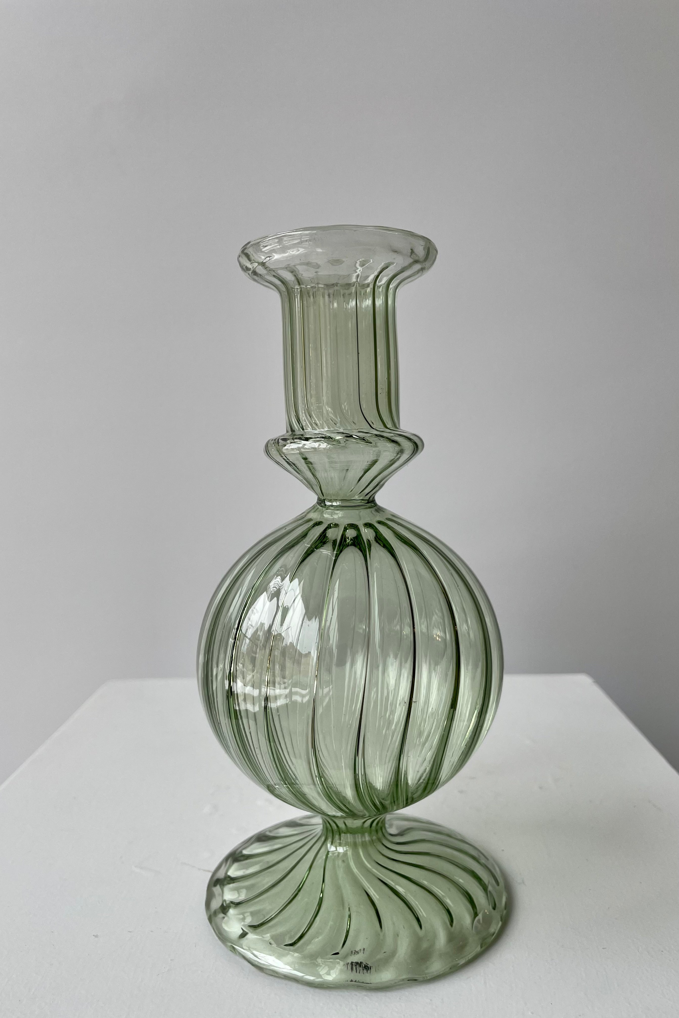 Photo from front of green transparent glass of Nalia Parakeet Candlestick Hollder against a white wall.