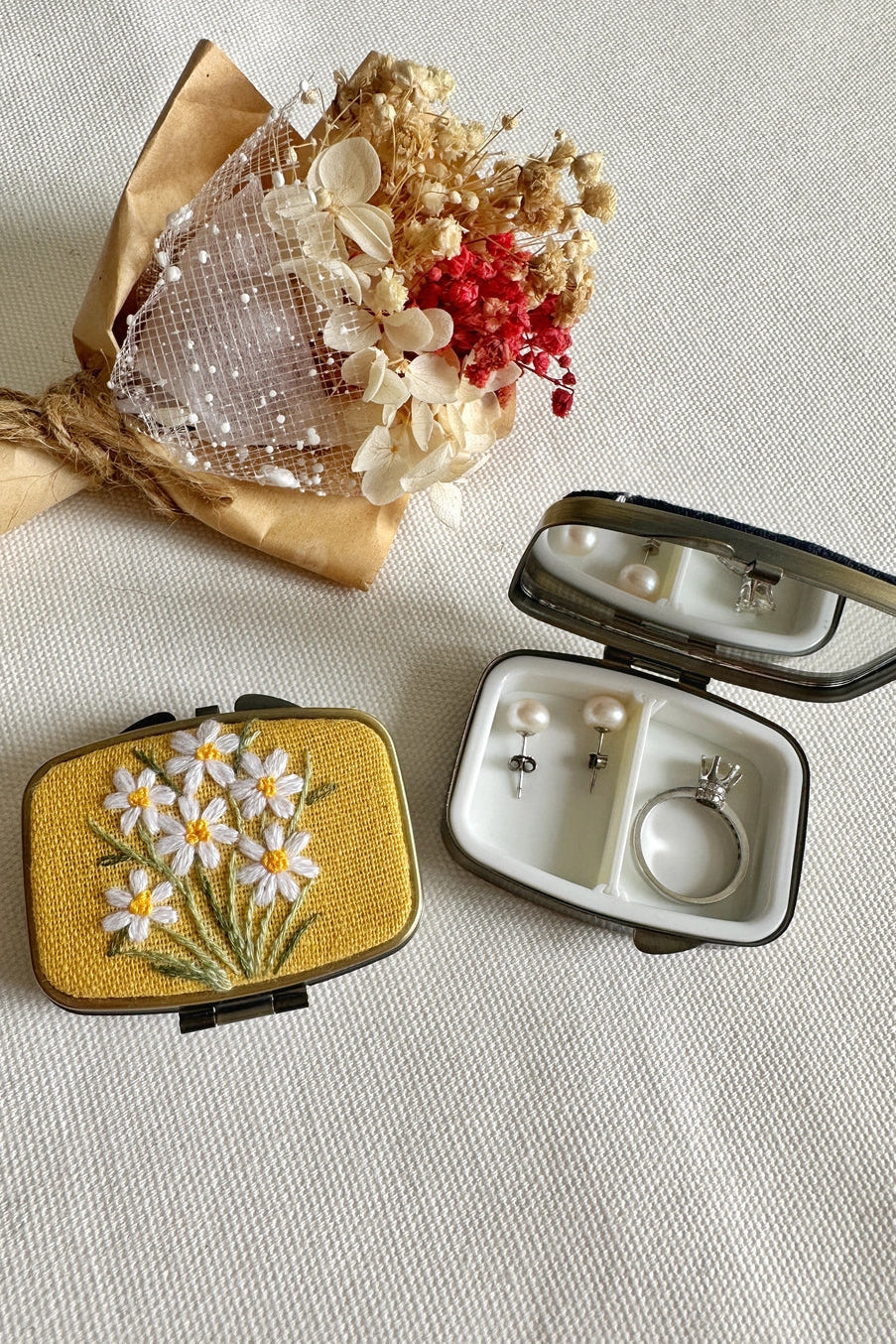 Small embroidered box with flowers and a jewelry case on a textured surface ©Quince Fables