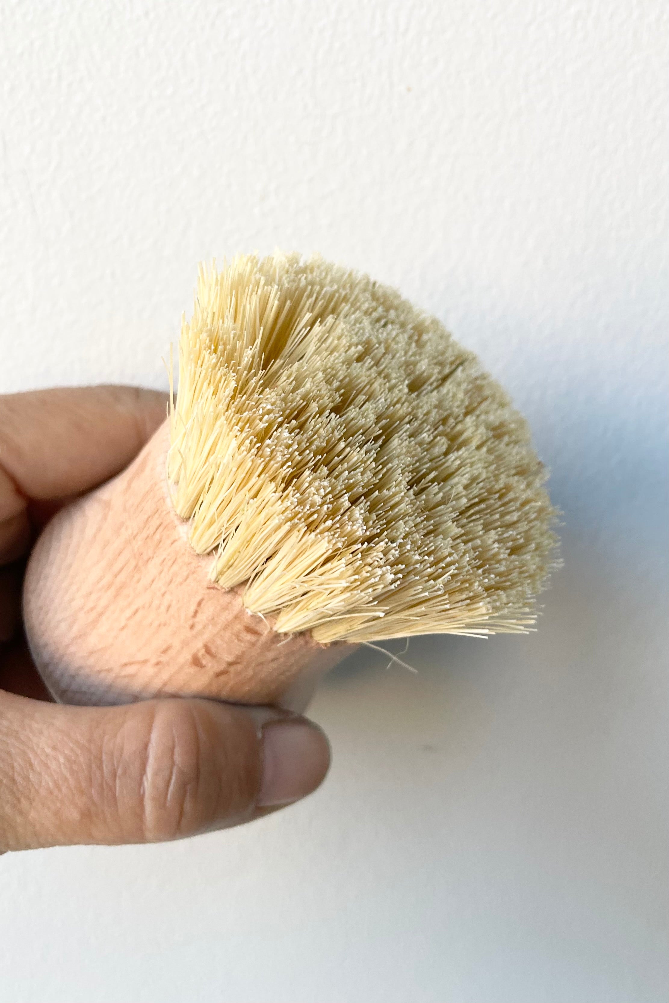 The beech wood natural brush being held in hand against a white wall.