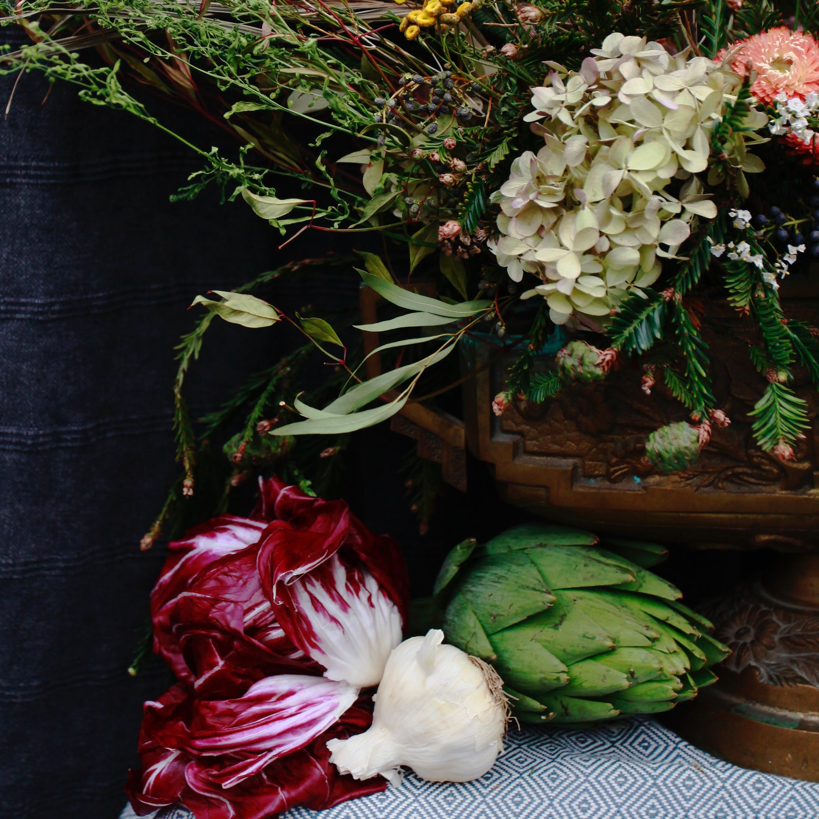Artichoke, radicchio, and other vegetables with a floral arrangement on a dark background ©Sprout Home