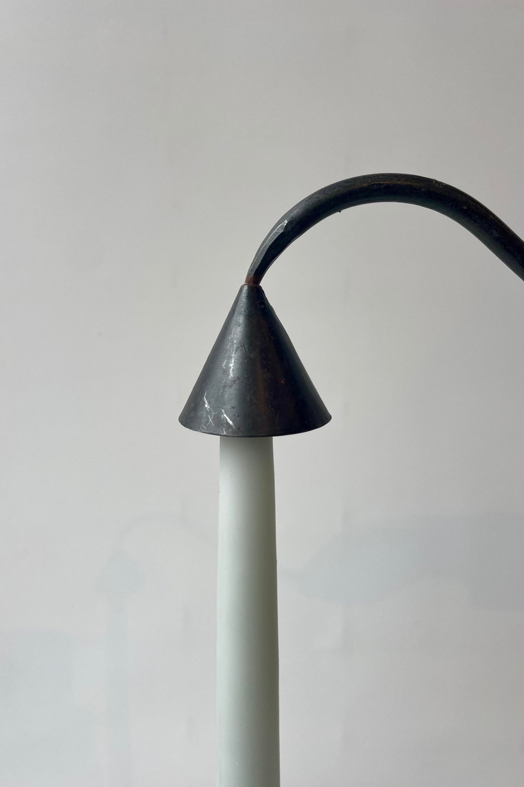 Close photo of a black metal candle snuffer placed over the tip of a pale blue taper candle. The object pair is shown against a white wall. ©Sprout Home
