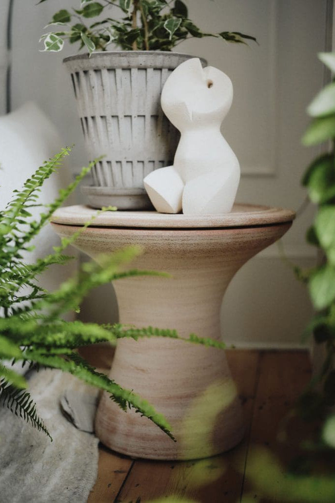 A potted plant and white sculpture on a clay table with a neutral background and plants ©Bergs Potter