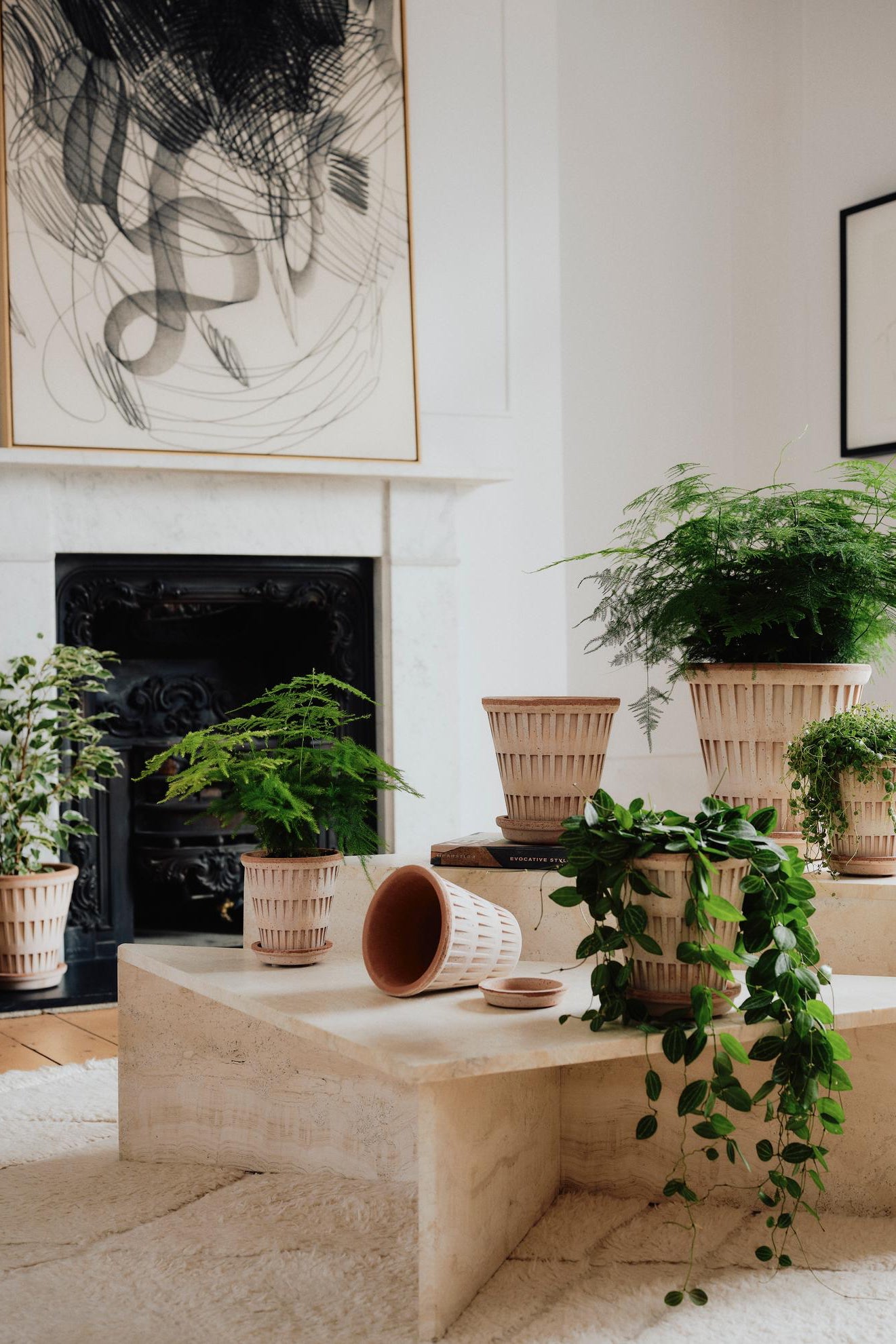 Modern living room with a fireplace, potted plants in Pantheon planters, and abstract art. ©Bergs Potter