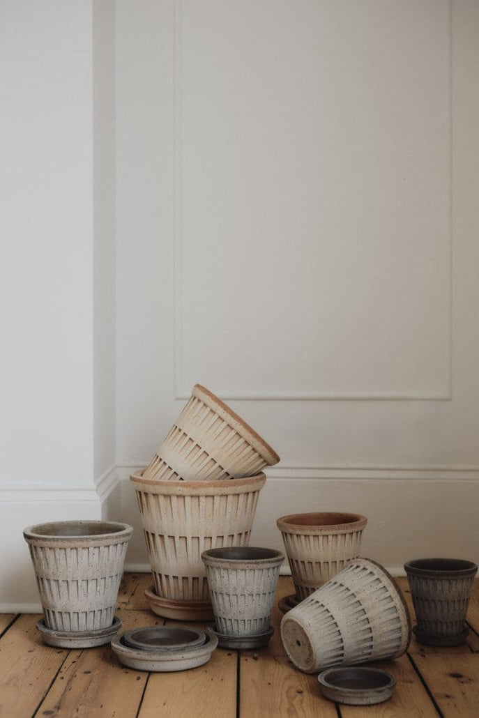 A collection of terracotta and gray clay pottery and saucers on a wooden floor in a white room. ©Bergs Potter