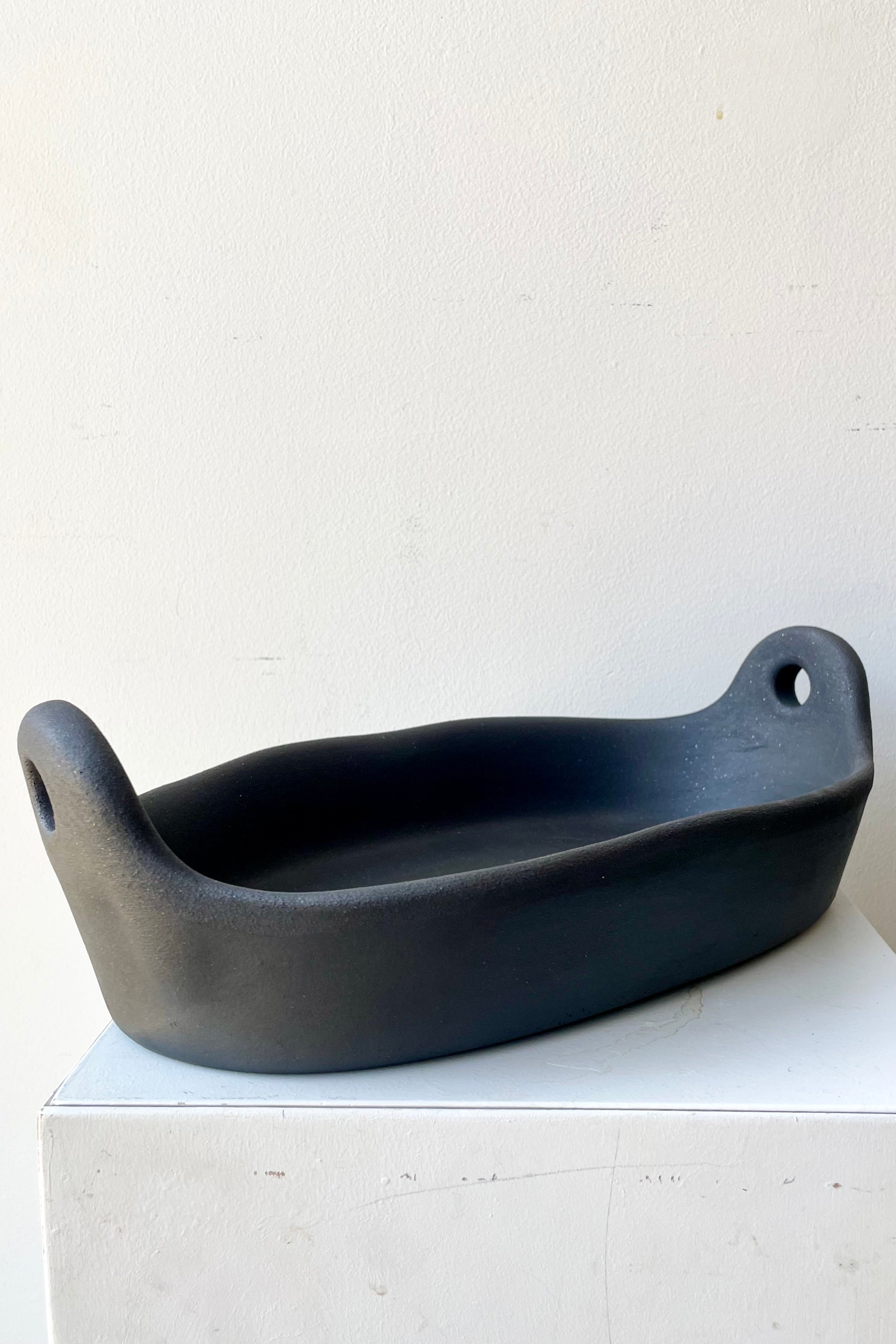 The small Barro oval roaster sitting on a white stand against a white wall.