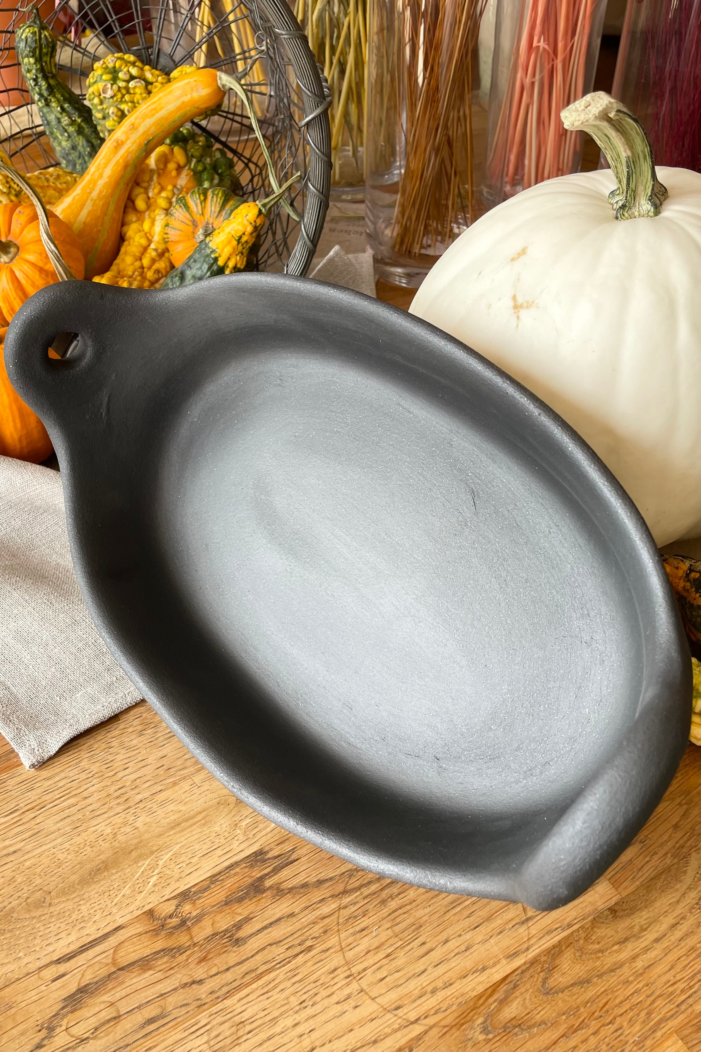 Small Barro oval roaster laying on its side on a wood table with some gourds in the background.