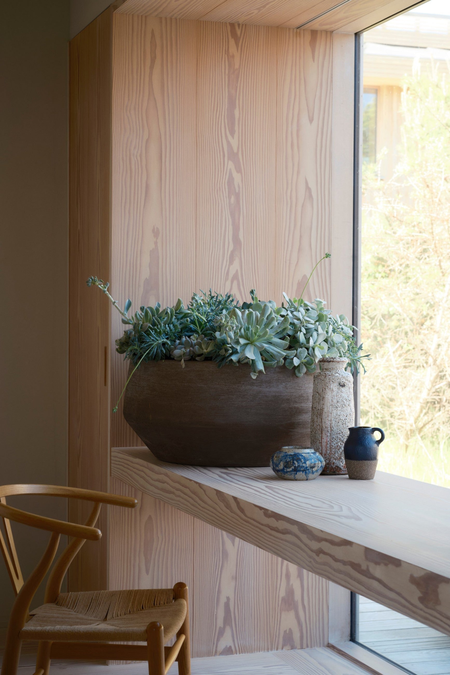 Decorative setup with potted plants in a Doma Grey planter on a windowsill in a room with wooden walls and a chair ©Bergs Potter