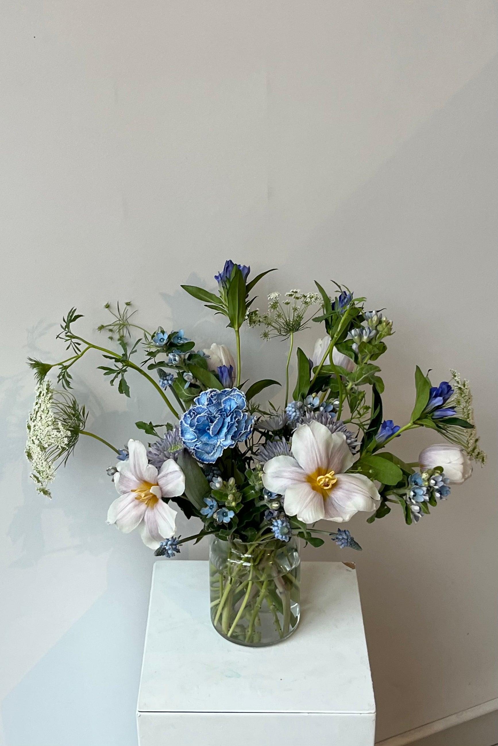 Photo of floral arrangement on a white surface in front of a white wall at Sprout Home. The flowers are various shades of blue, indigo, aqua and teal. ©Sprout Home #size_$100
