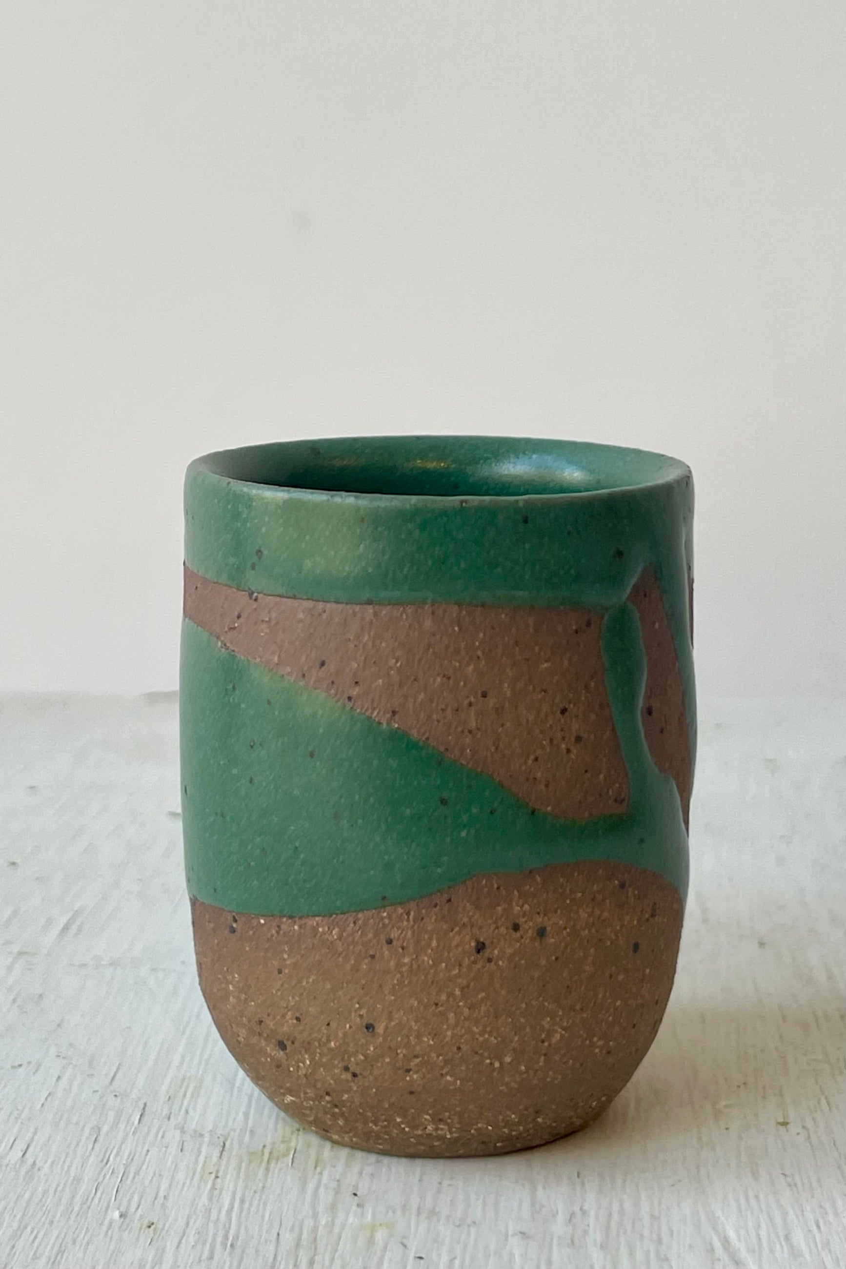 Photo of a small cup with a brown clay and green glaze pattern in front of a white wall ©Sprout Home