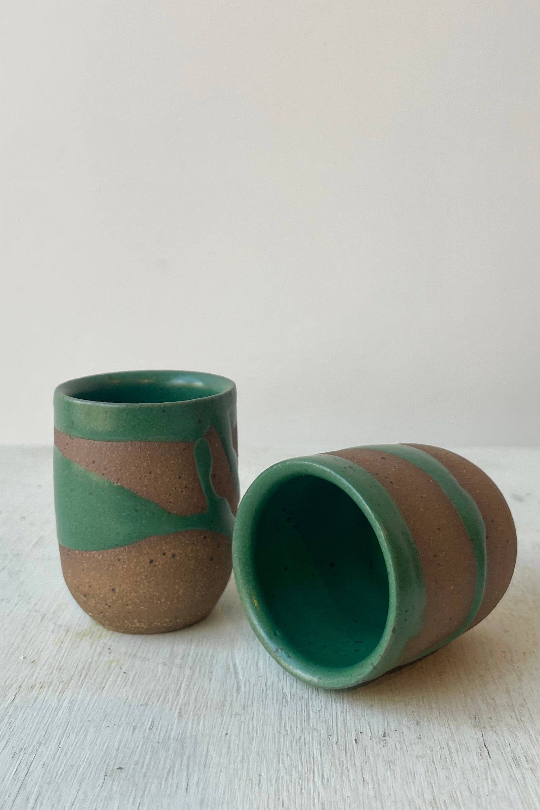 Photo of a pair of small cups with a brown clay and green glaze pattern in front of a white wall ©Sprout Home