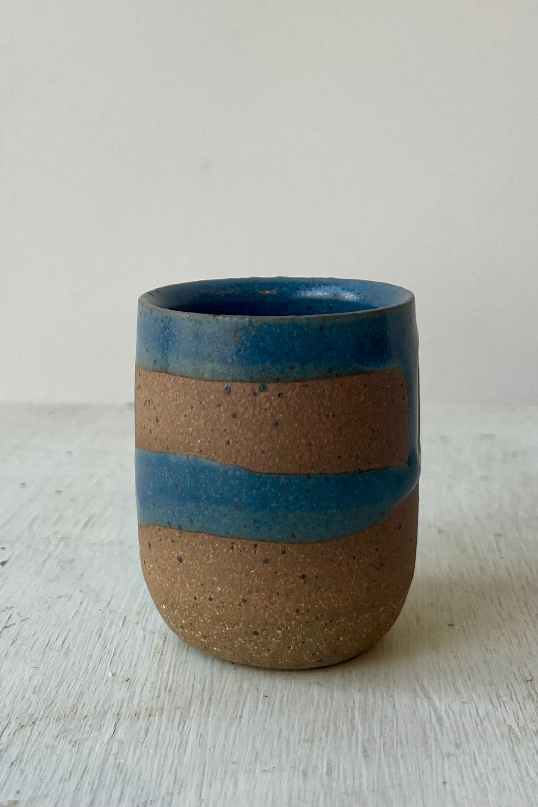 A small ceramic cup with brown clay and a dark blue glaze in front of a white wall ©Sprout Home
