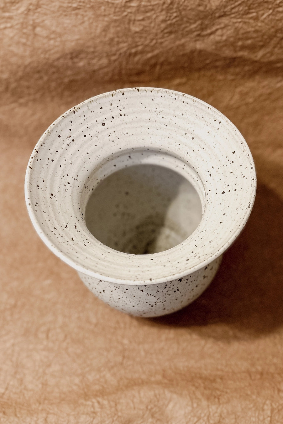 Flared Cornwall Stone vase on a textured brown surface ©Olivia Snow Ceramics