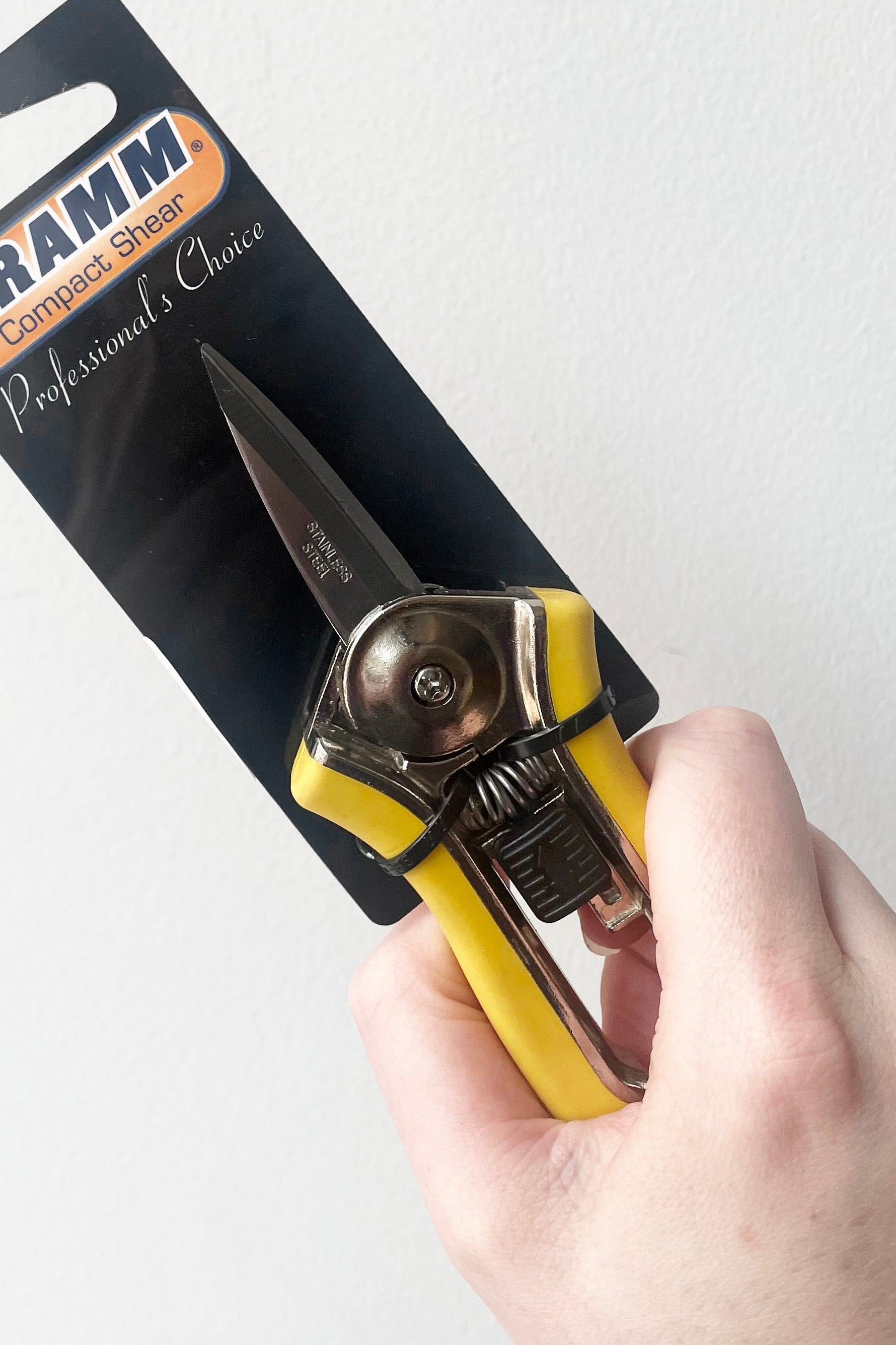 A hand holds Dramm Color Point Compact Shear against white backdrop
