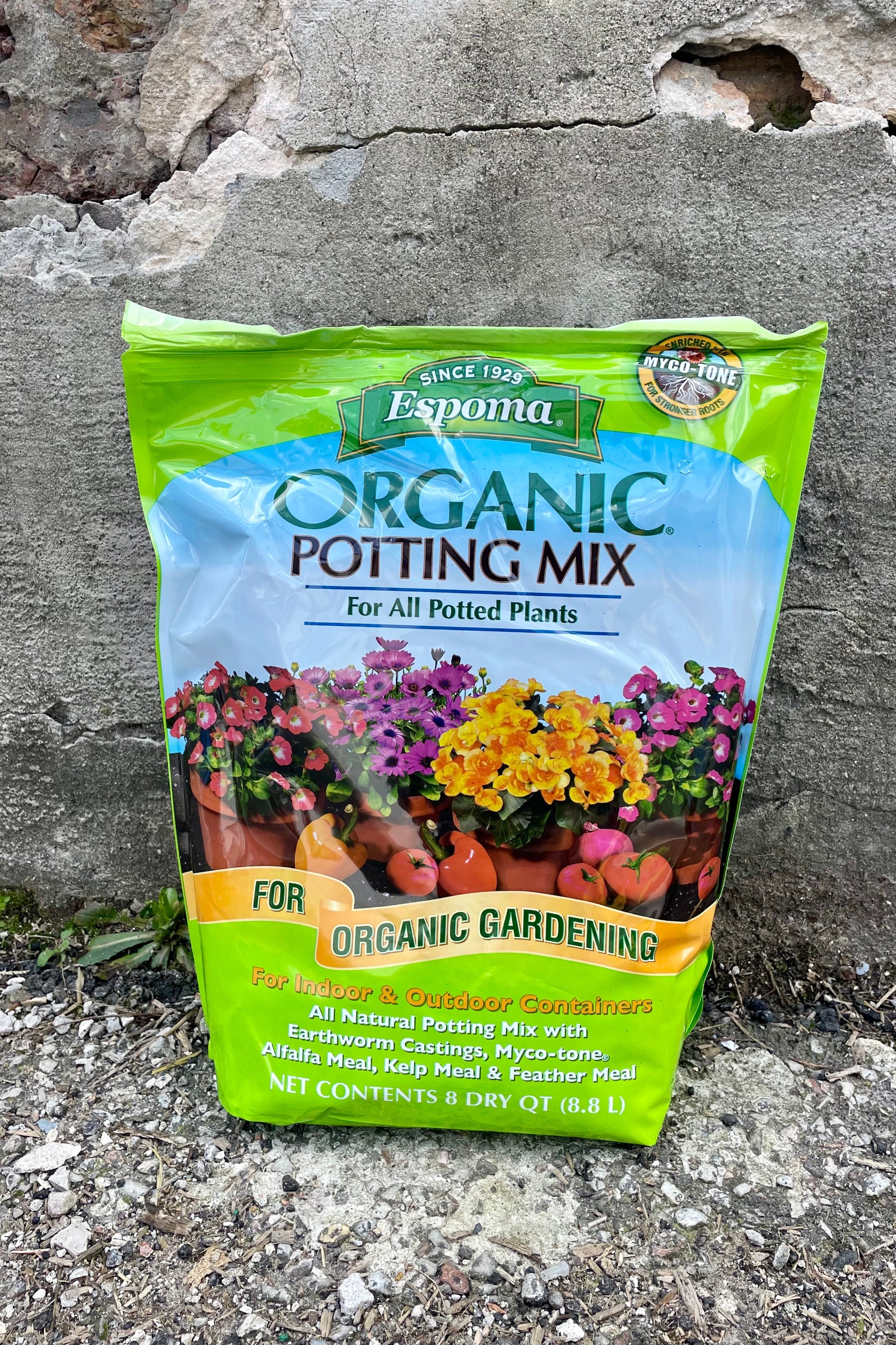 Photo of a plastic bag of organic potting mix against a cement wall. The bag is bright green with a middle band of illustration and text showing the product name and images of flowers and vegetables with the text "for organic gardening." The bottom text shows the contents and volume of the bag. ©Sprout Home