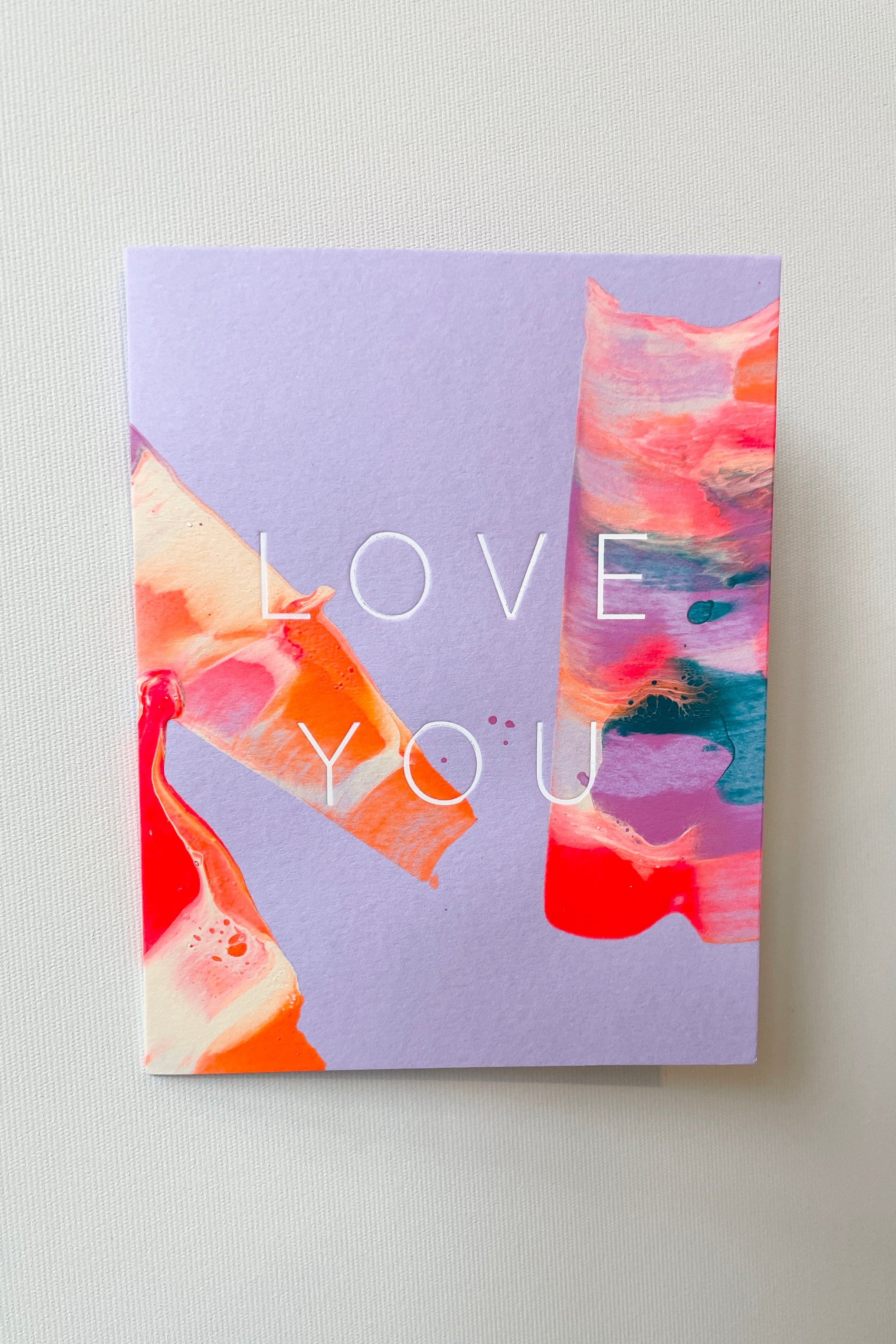 The Orchid Love You Card by Moglea shown from the front on a white wall.