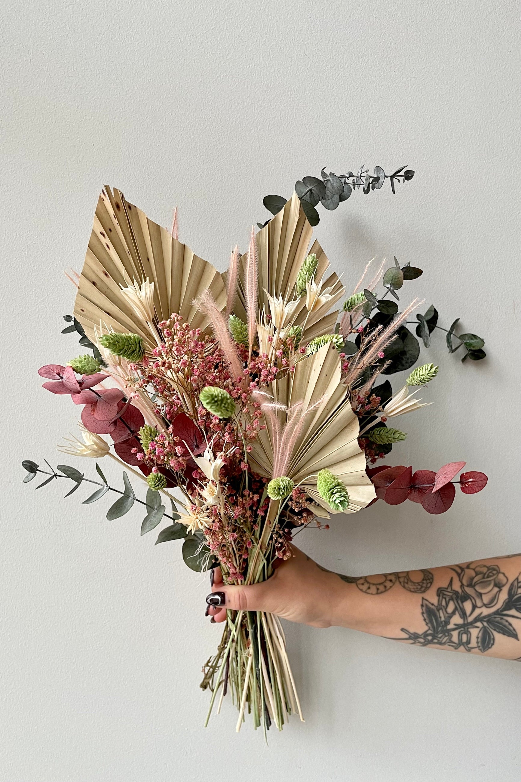 'Faerie' dried floral arrangement by Sprout Home being held against a white wall showing off its neutral and pastel palette. ©Sprout Home #size_$85